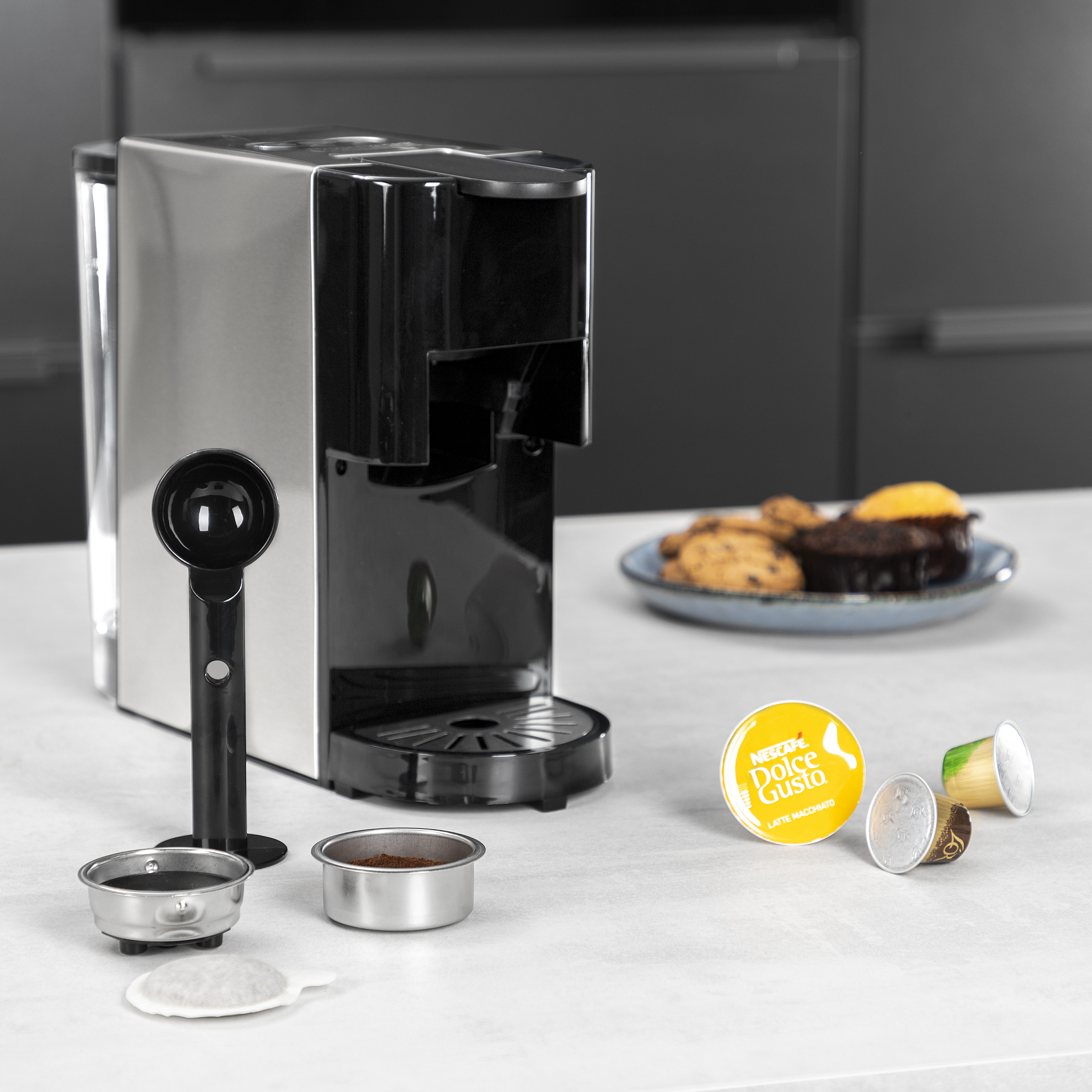 Espressomachine met accessoires en koffiepads. Koekjes op de achtergrond.