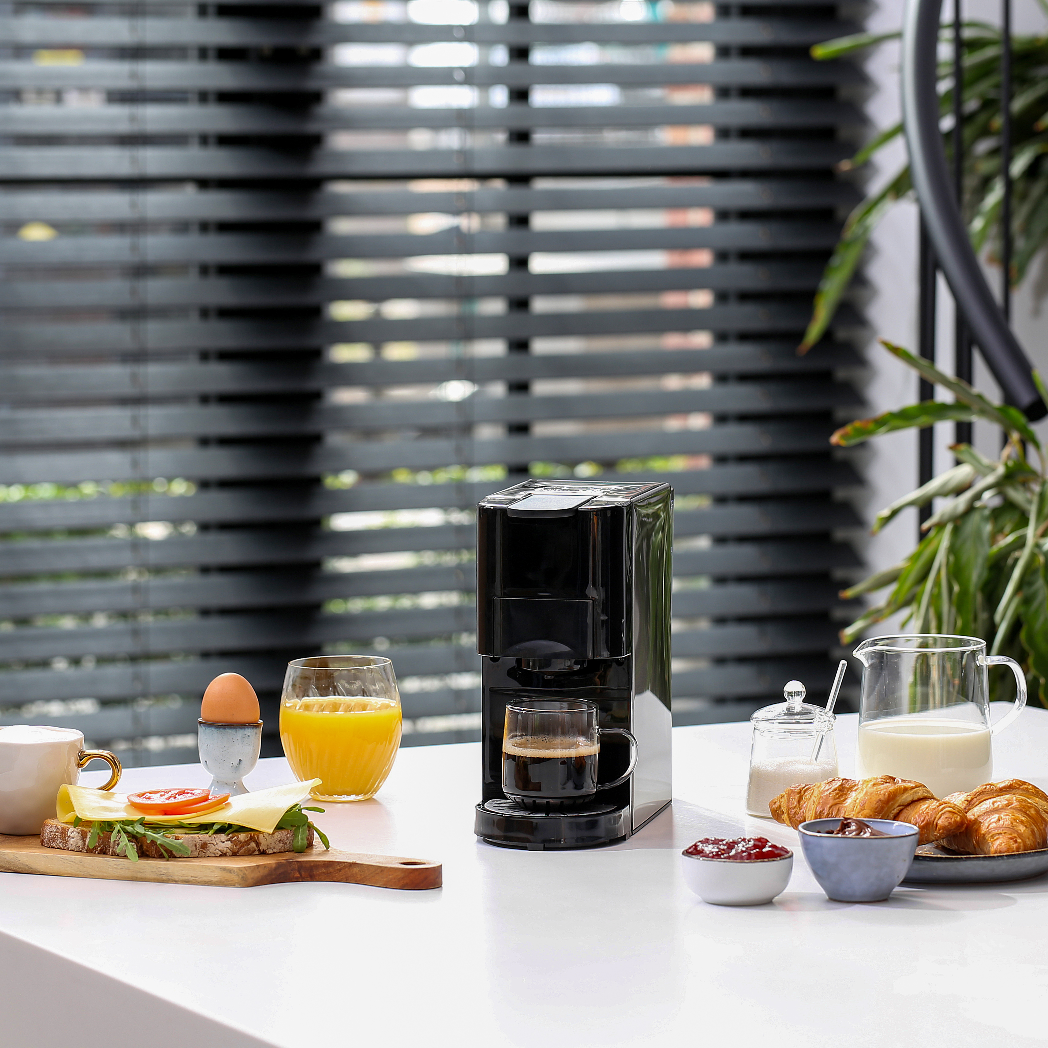 Ontbijt: koffie, sap, brood, ei en croissants op een witte tafel. Zwart koffiezetapparaat.