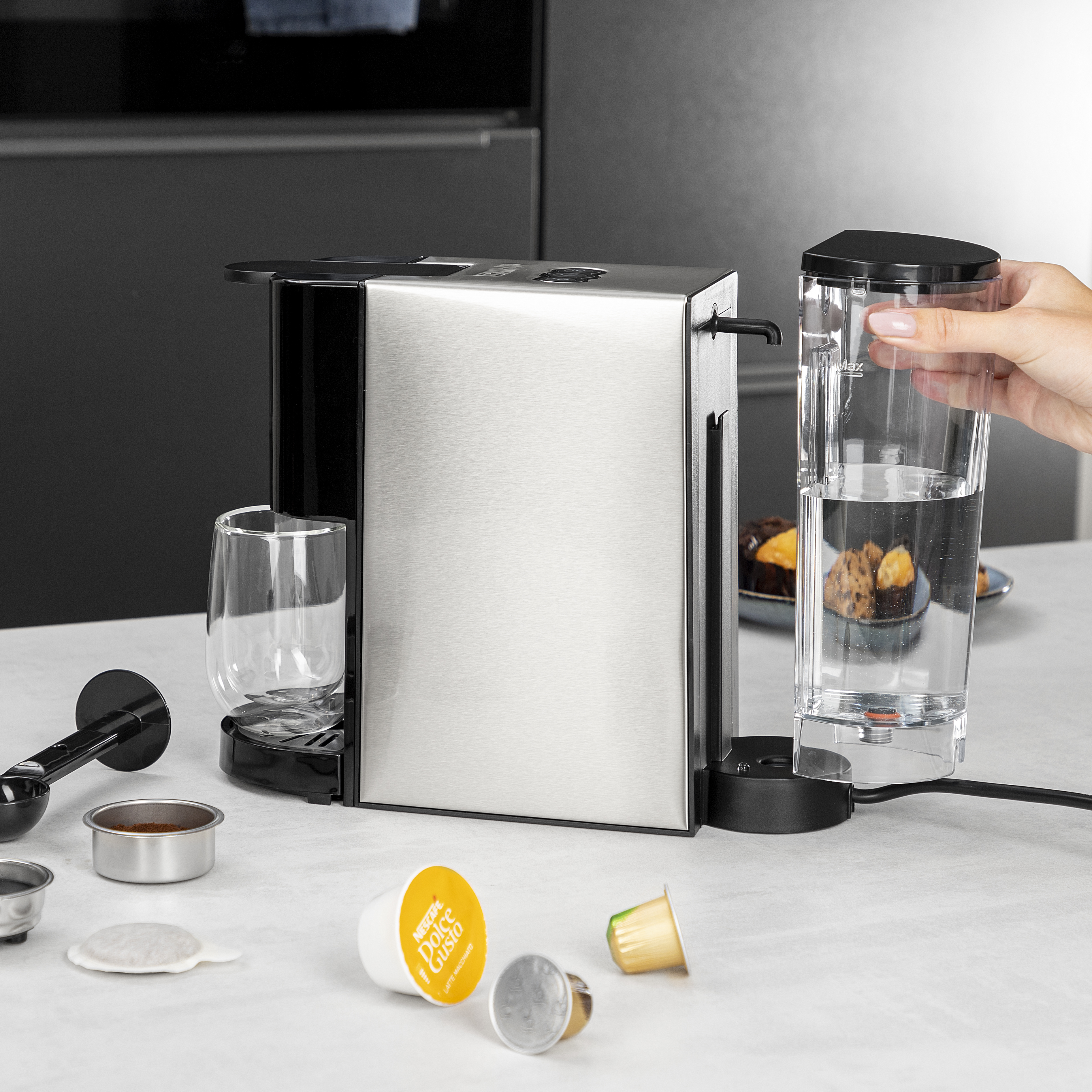 Een koffiemachine met accessoires. Een persoon houdt een watercontainer vast.