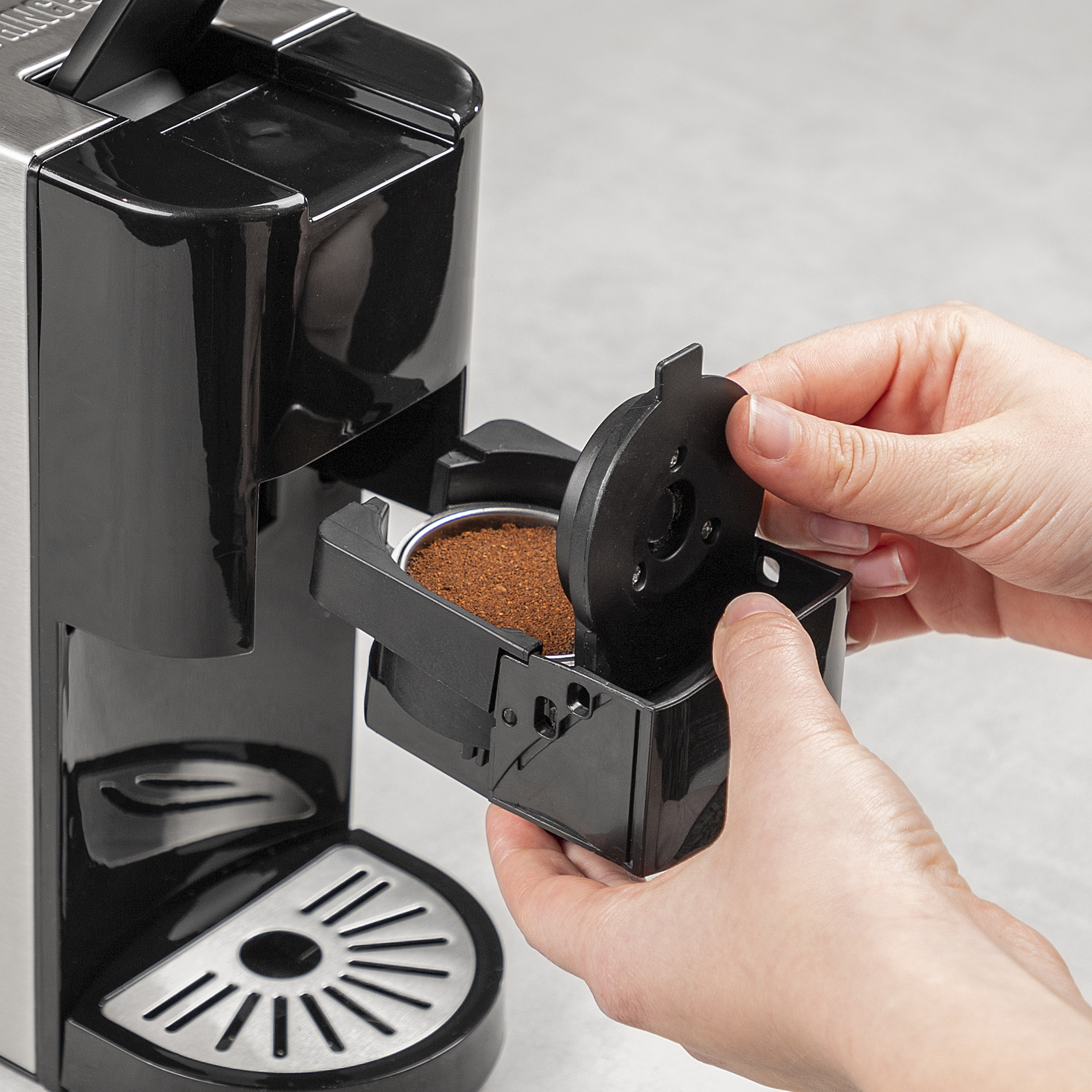 Een persoon verwijdert de filterhouder van een zwart-zilveren koffiemachine.