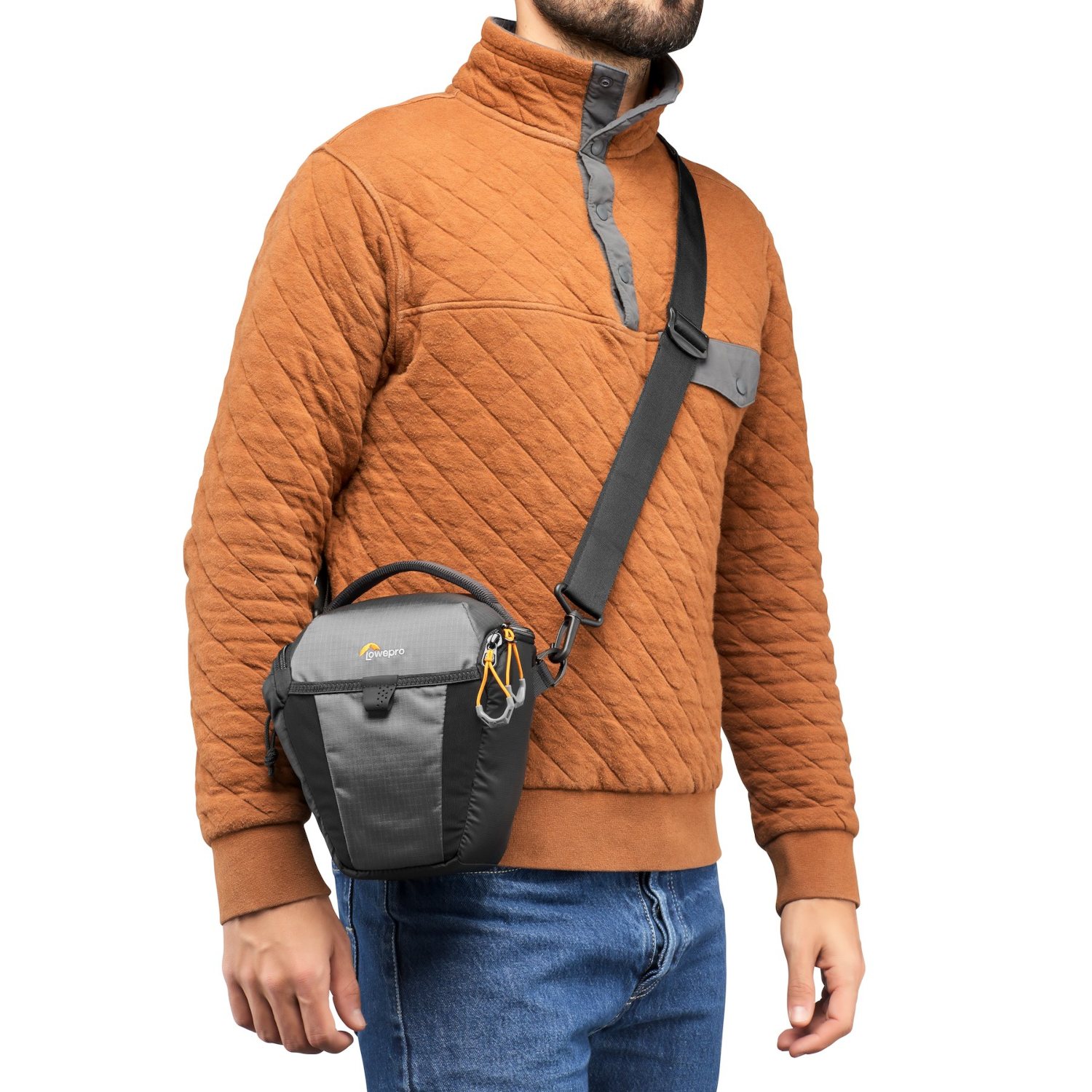 A man with a camera bag over his shoulder, in front of a brown background.