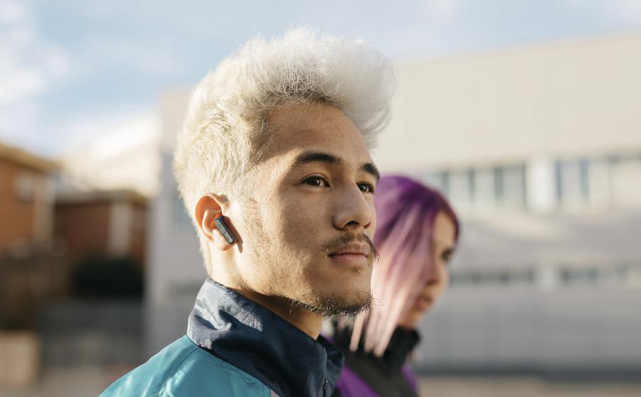 Ein Mann mit silbernen Haaren, der einen Ohrhörer trägt, eine weitere Person im Hintergrund.