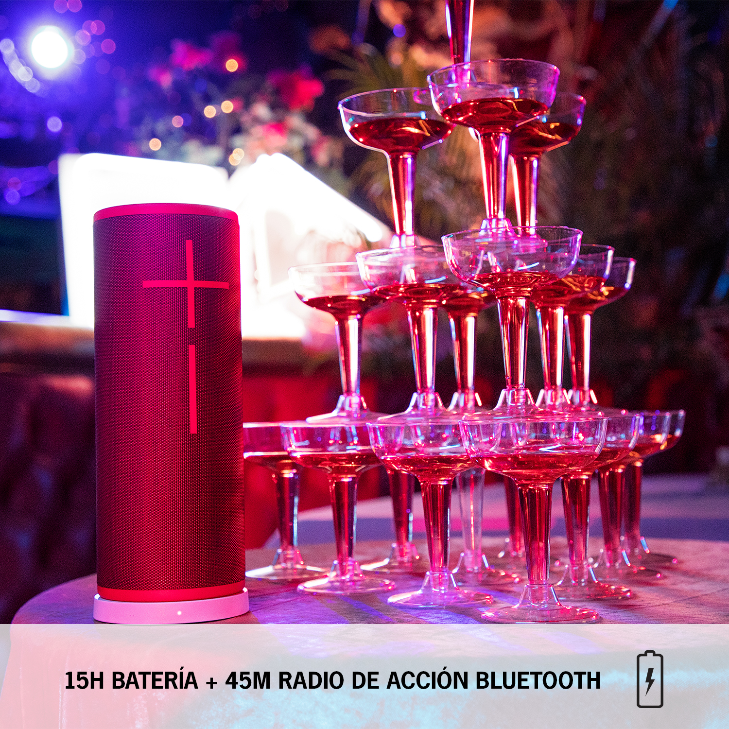 Un altavoz rojo con base clara, junto a una pila de copas de champán sobre una mesa.