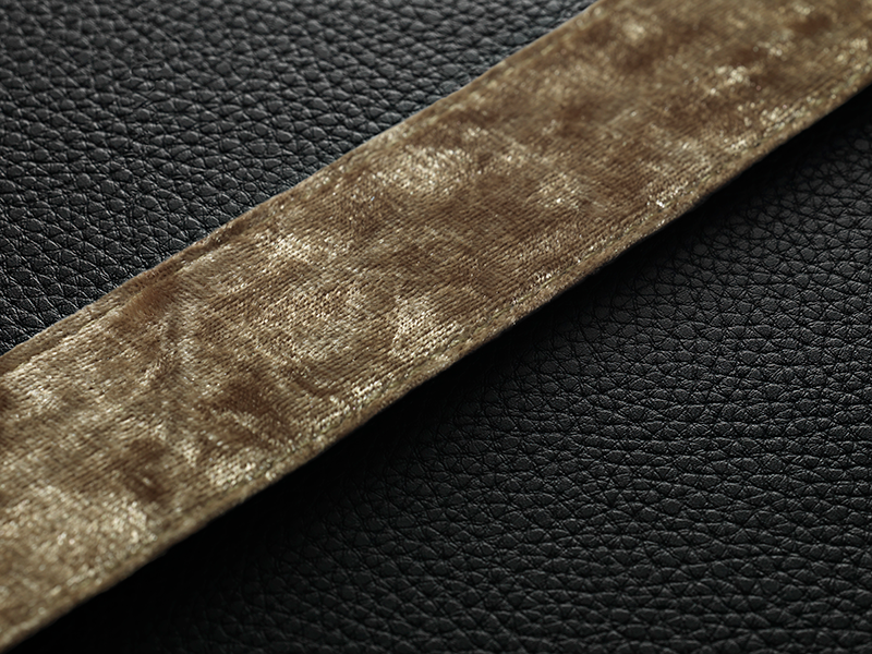 Close-up of a brown velvet ribbon on a black leather surface. Texture is visible.