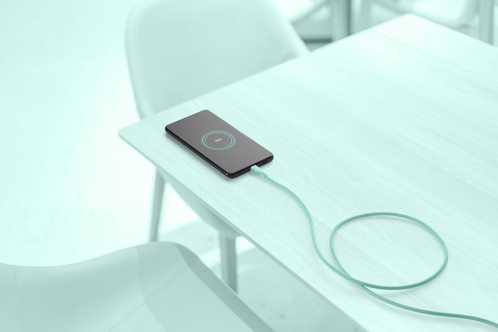 Ein Smartphone, das auf einem hellblauen Tisch mit einem Ladekabel geladen wird.