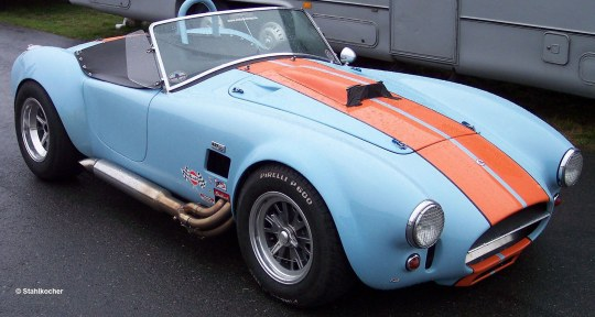 Hellblaues klassisches Auto mit orangenen Streifen. Auf nassem Untergrund geparkt. Metallaustritt sichtbar.