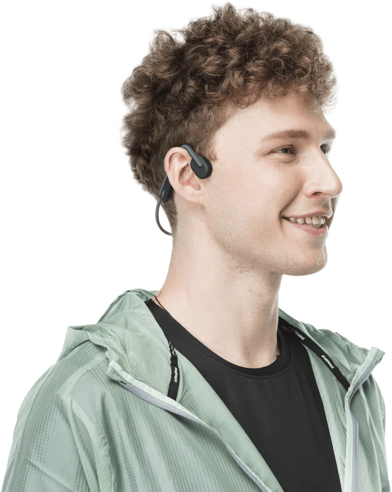 Un homme portant un casque à conduction osseuse, souriant, dans une veste verte.