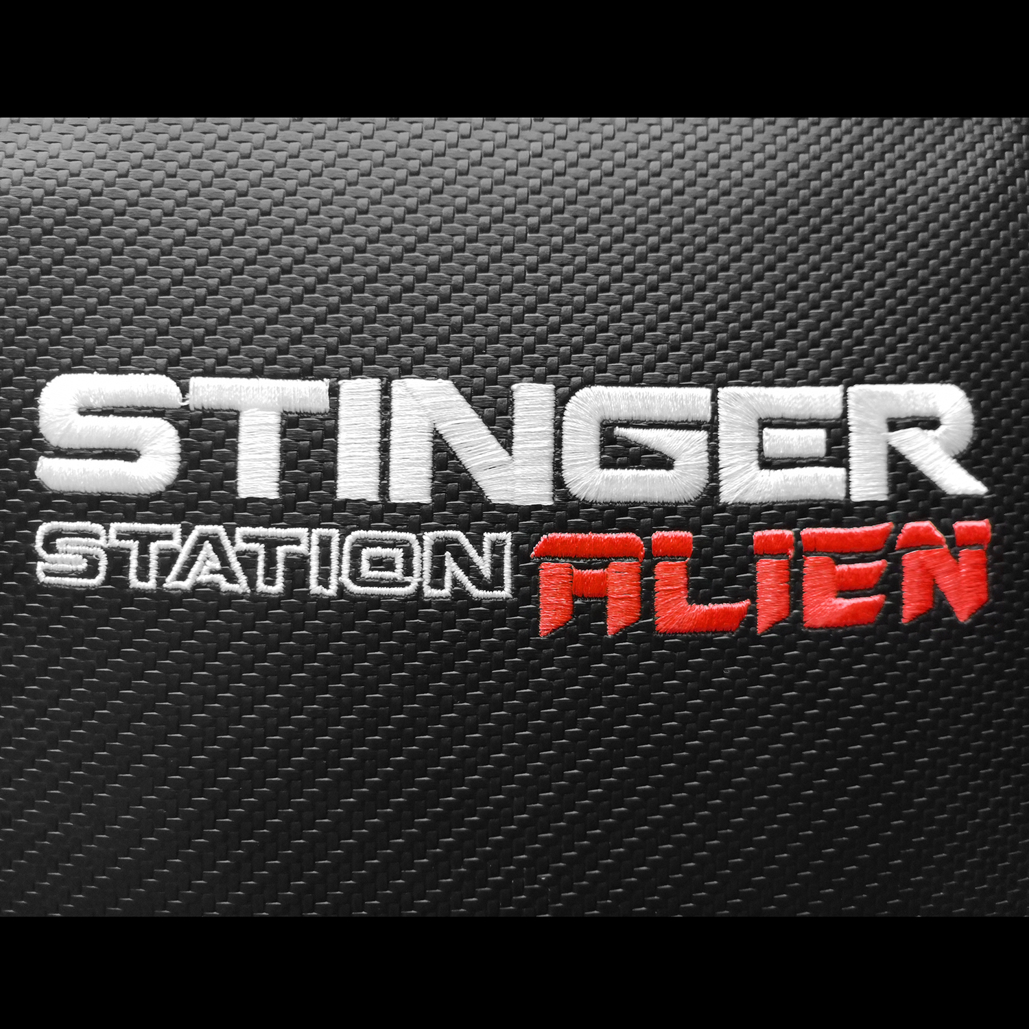 Primer plano de tela negra con texto bordado blanco y rojo: STINGER STATION ALIEN.