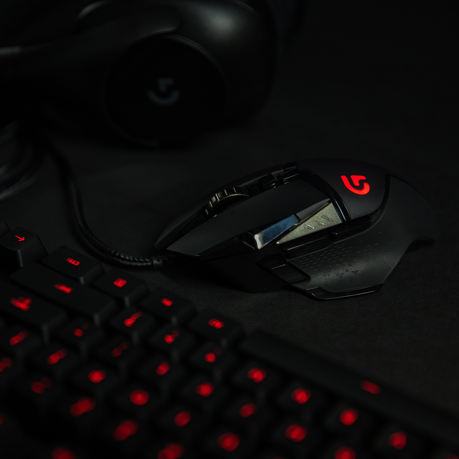 Configuración de juego con ratón, teclado y auriculares negros, todo sobre una superficie oscura con luces rojas.