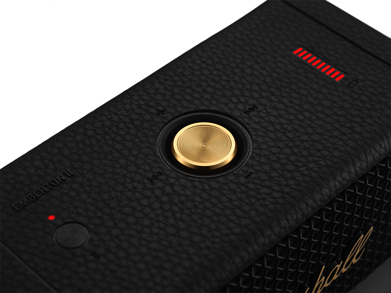 A close-up of a black speaker with a gold button and a red light.