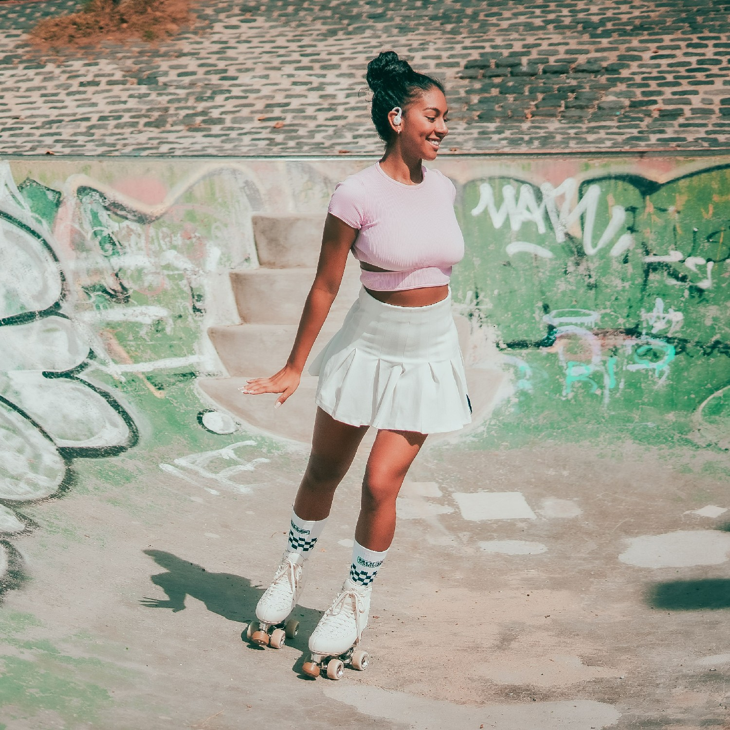 Mujer en patines en un parque de skate, con top rosa y falda blanca, sonriendo.