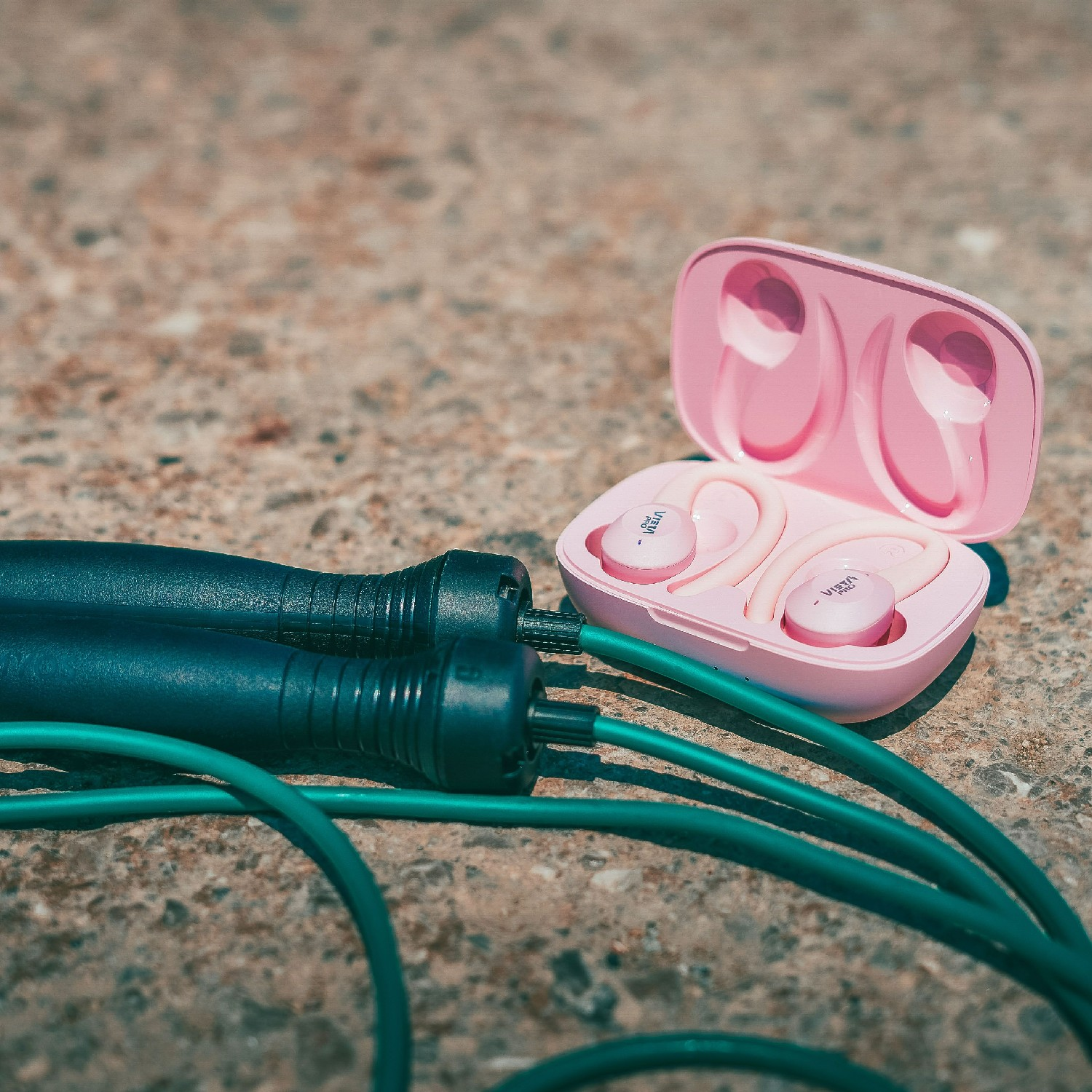 Auriculares rosas en estuche y una cuerda para saltar sobre concreto.