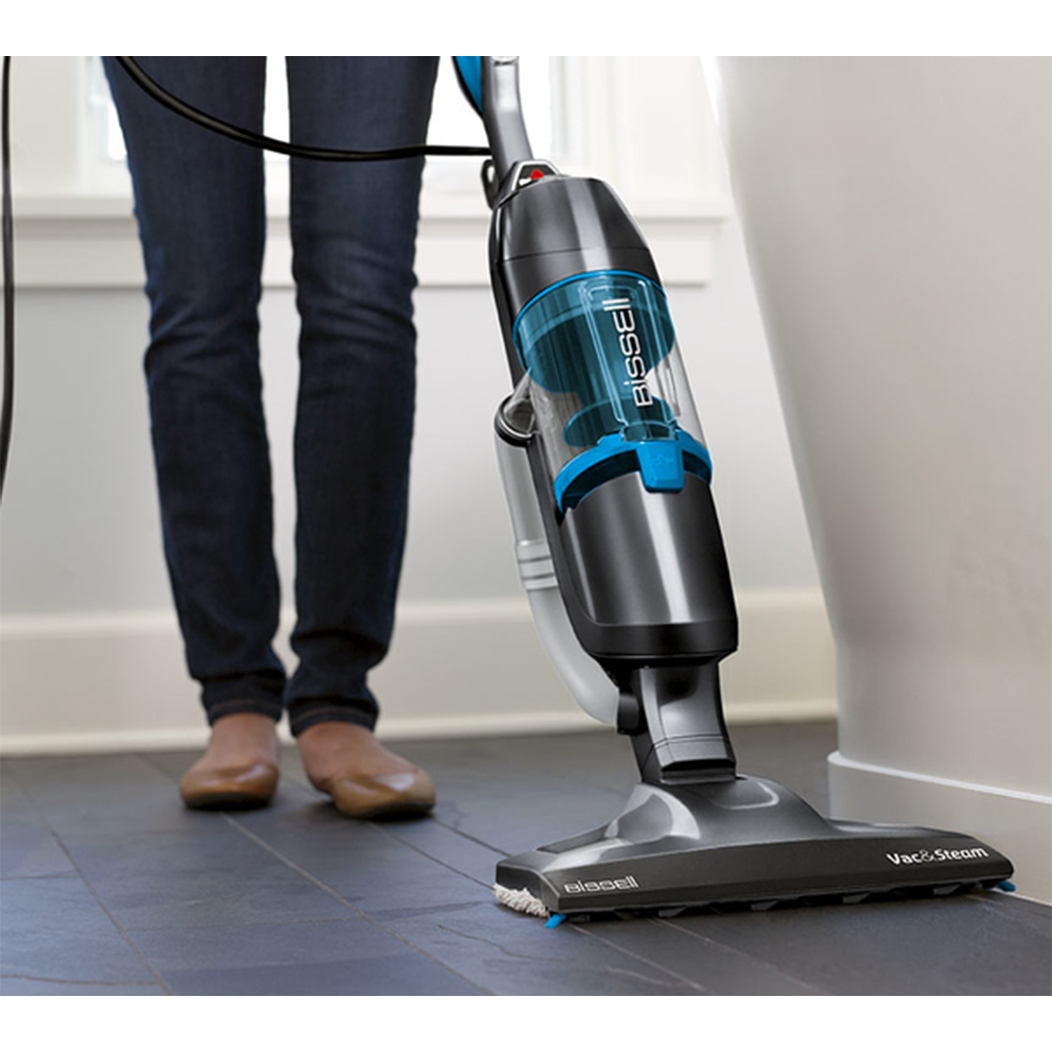 Una scopa a vapore e una persona con jeans blu e scarpe marroni stanno pulendo.