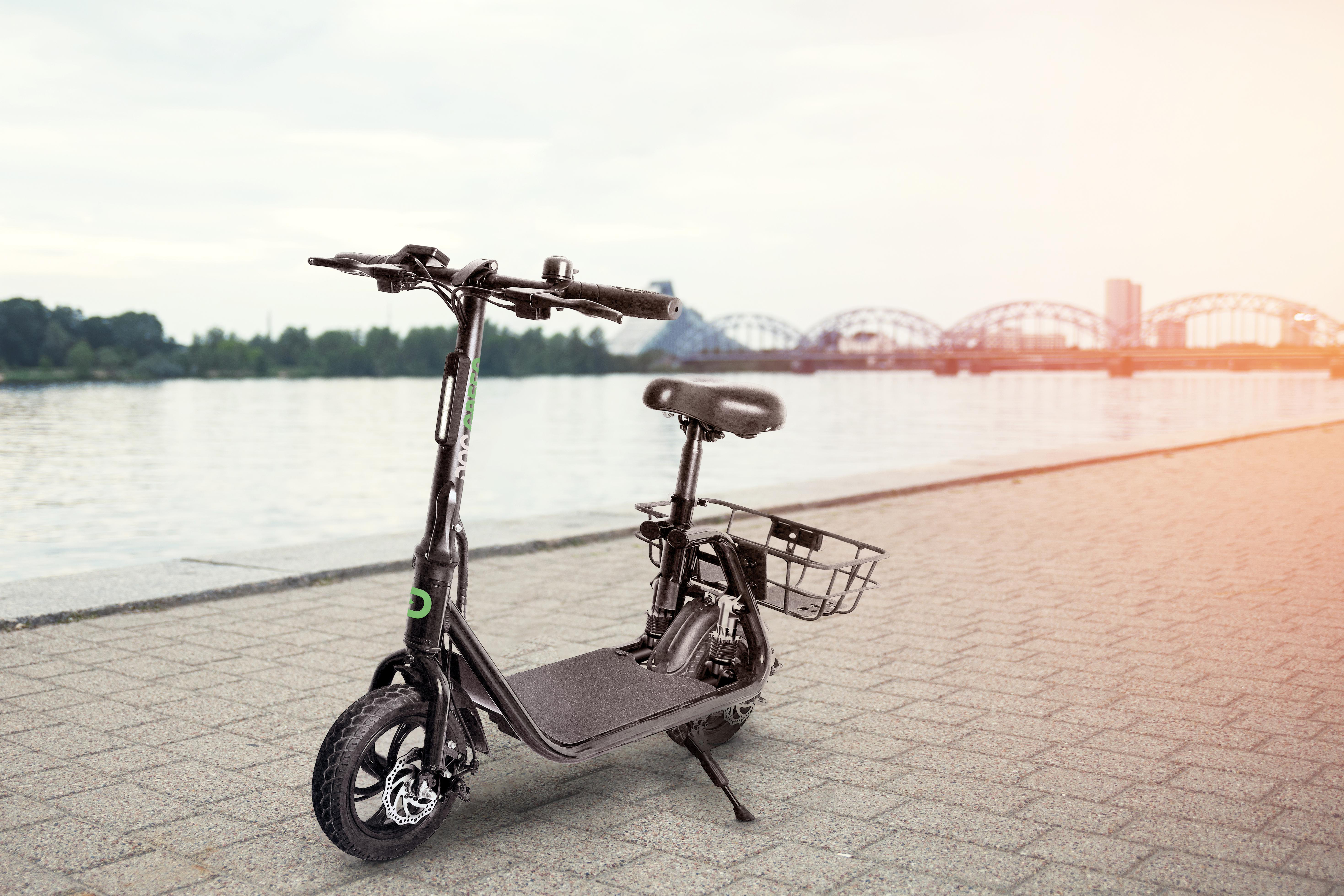 Schwarzer Elektroroller, geparkt auf einer gepflasterten Fläche am Wasser.