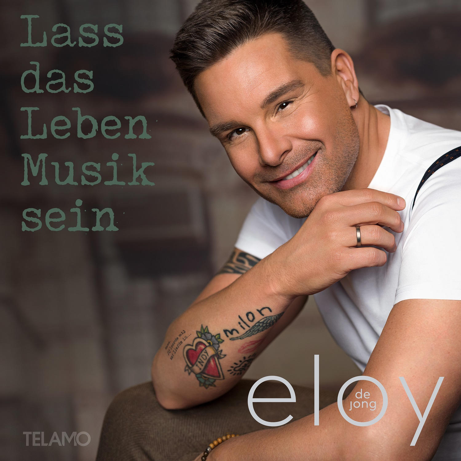 Ein Mann mit Tattoo lächelt, der Text lautet 'Lass das Leben Musik sein'.