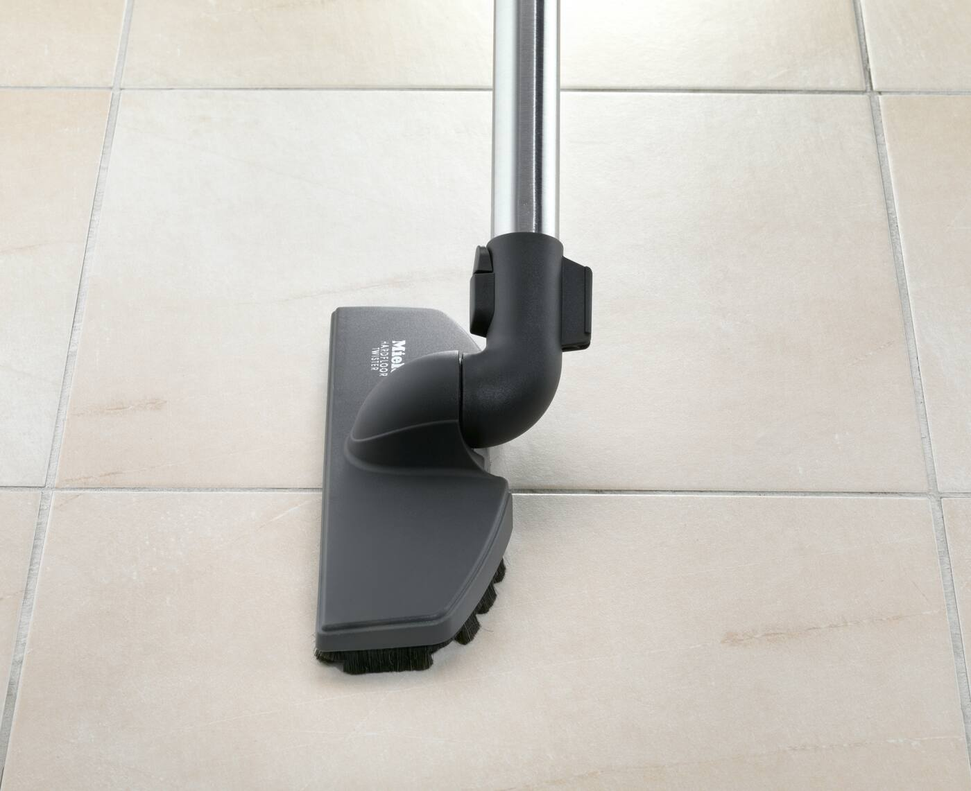 Tête d'aspirateur sur sol carrelé. Montre brosse et partie du tube métallique.
