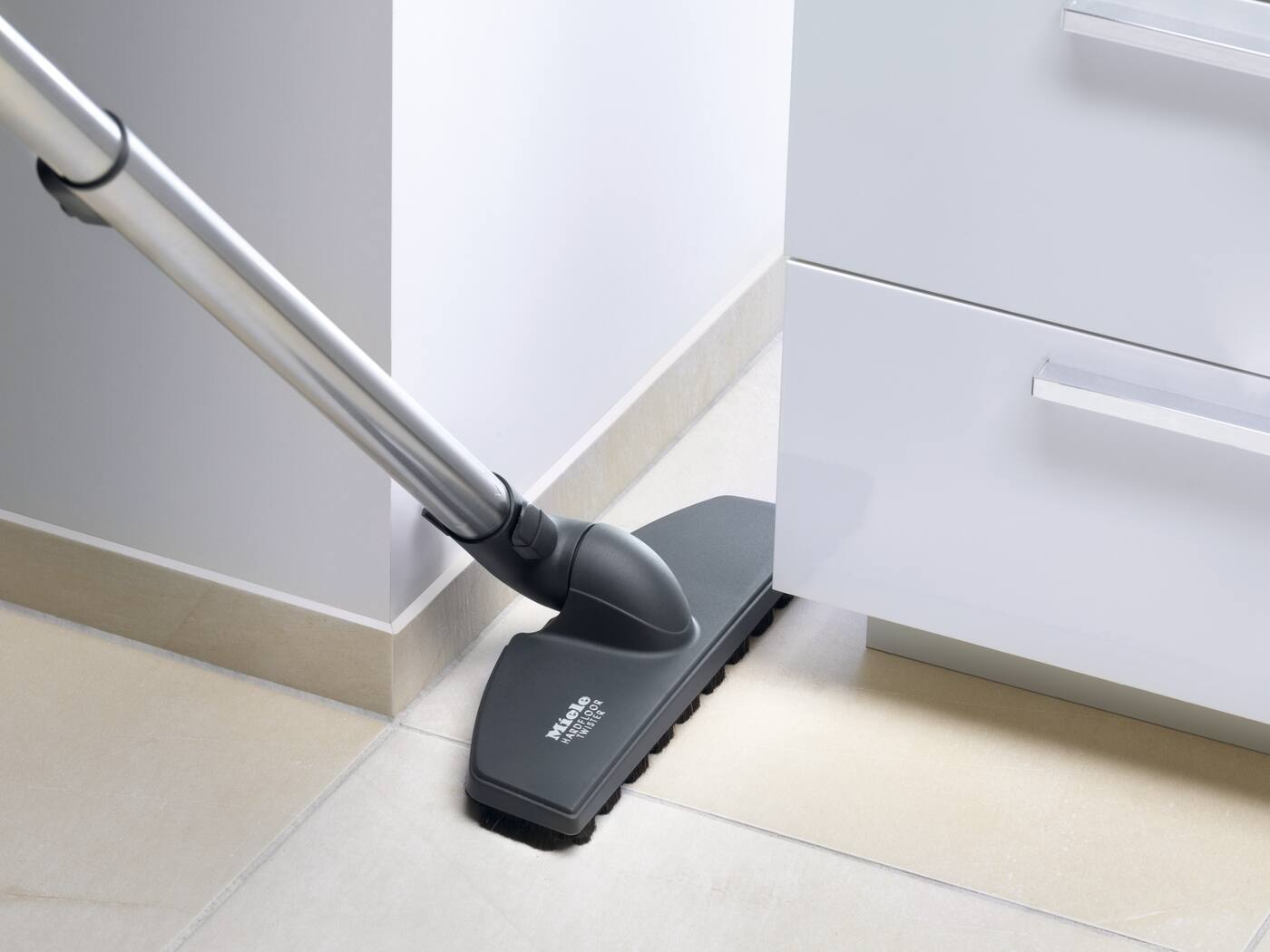 Buse d'aspirateur nettoyant le coin d'une pièce à côté d'une armoire.