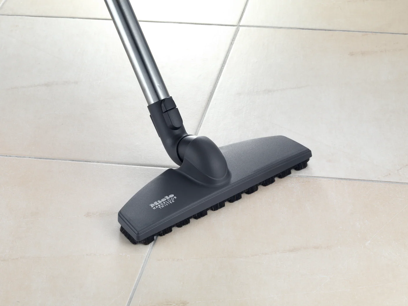 Tête d'aspirateur sur un sol carrelé, avec des poils de brosse visibles.