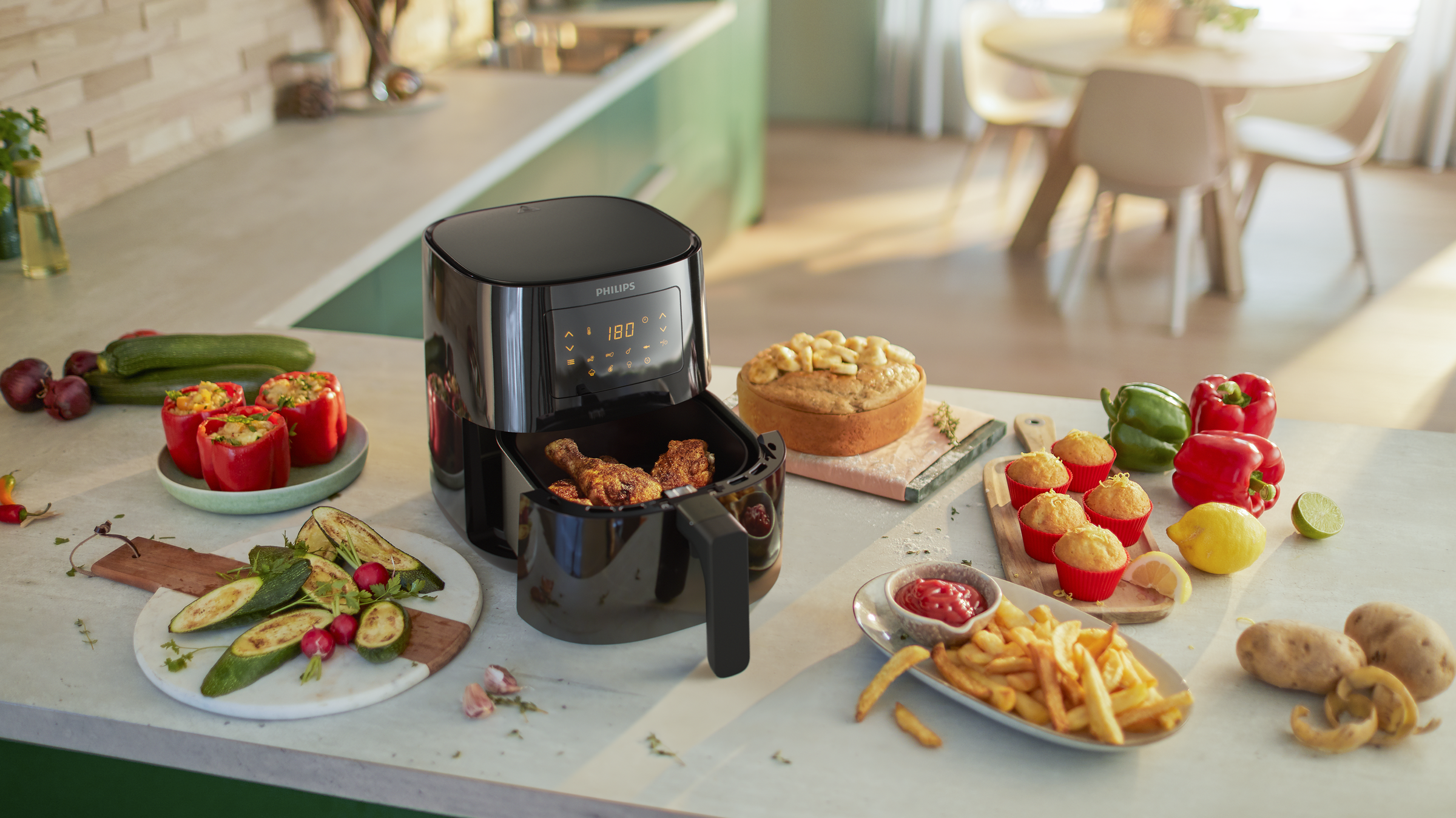 An air fryer with fried food, muffins, veggies, and condiments on a kitchen counter.