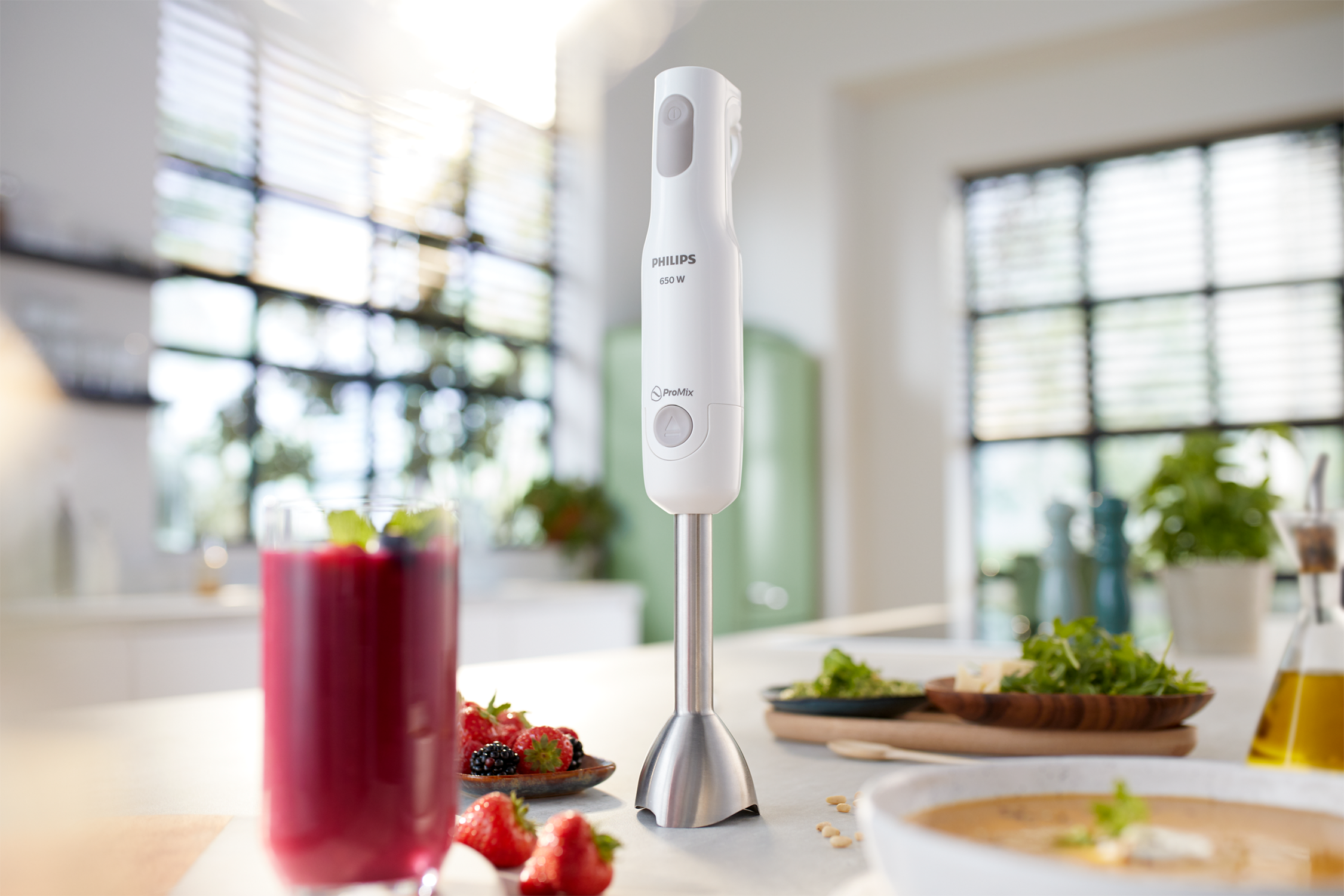 Witte Philips staafmixer met een glas paarse smoothie, ingrediënten en een soepkom.