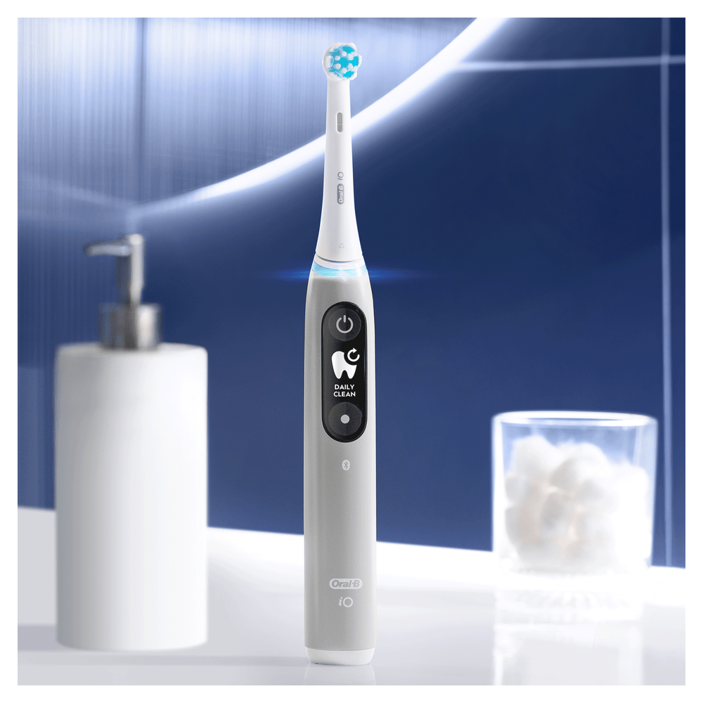 Cepillo de dientes eléctrico con pantalla, en un mostrador de baño, con jabón y un vaso.