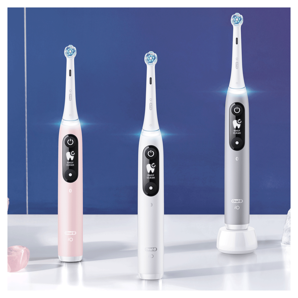 Tres cepillos de dientes eléctricos, rosa, blanco y gris, sobre fondo azul.