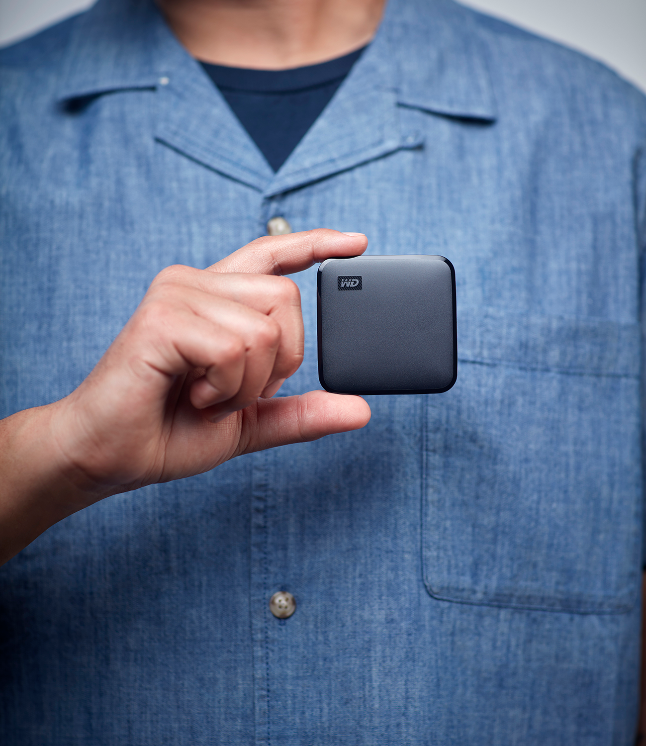A person holding a small, dark-colored, square device.