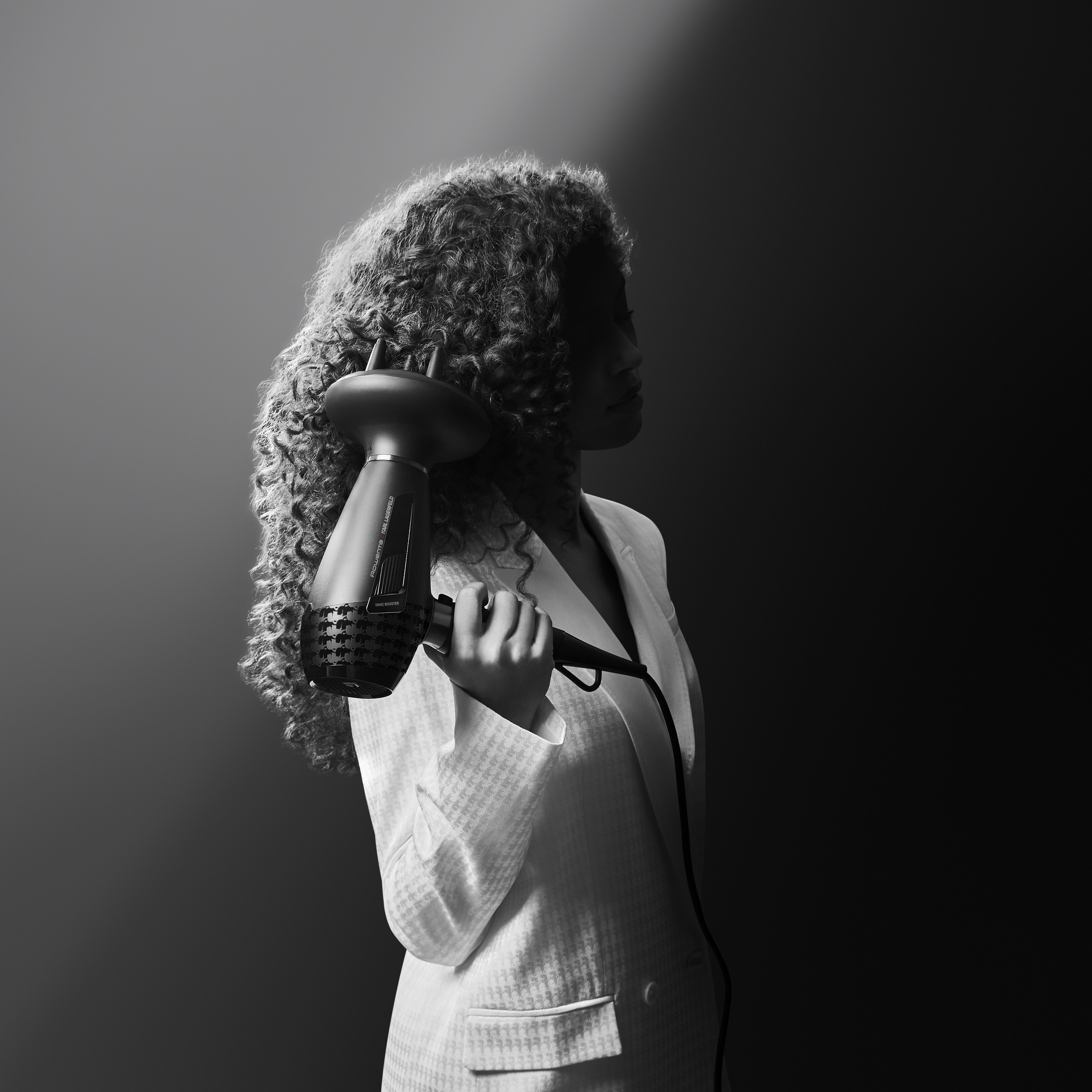 Mujer sosteniendo un secador de pelo con difusor. Foto en blanco y negro, fondo oscuro.