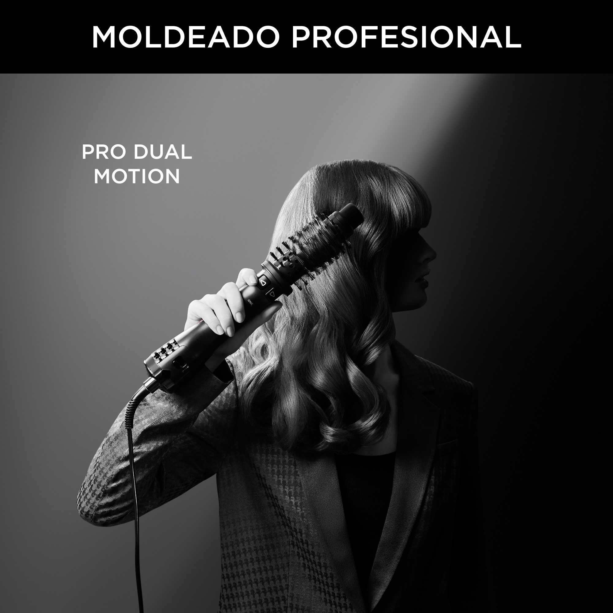 Mujer peinando el cabello con un moldeador negro, fondo oscuro.