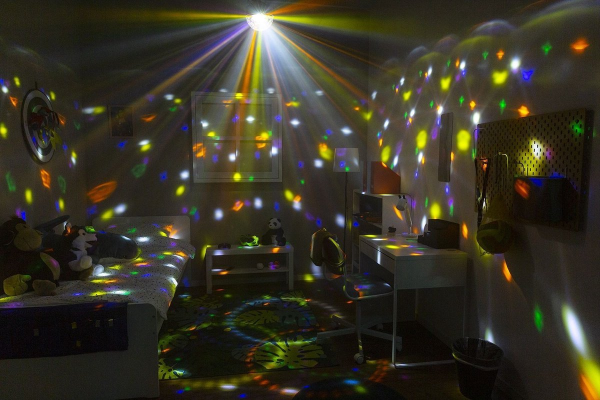 Chambre avec boule disco projetant des lumières colorées sur le lit, les murs et le sol.