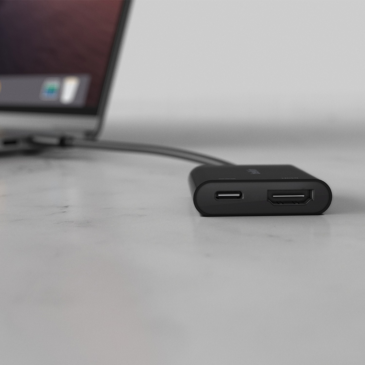 Concentrador USB-C negro conectado a una computadora portátil, con puertos HDMI y USB.