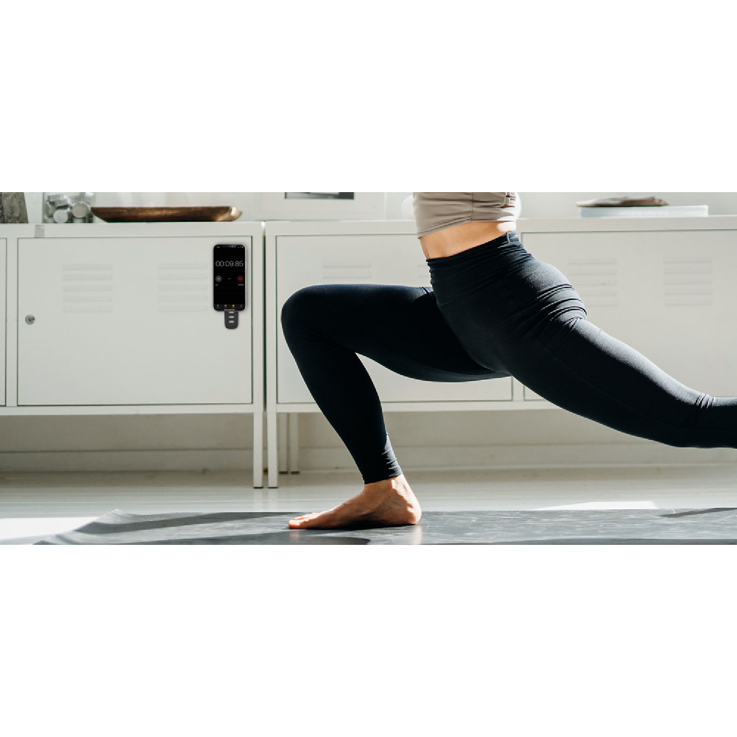 Mujer en pose de yoga con un temporizador en la pared. Mallas negras y un armario blanco.