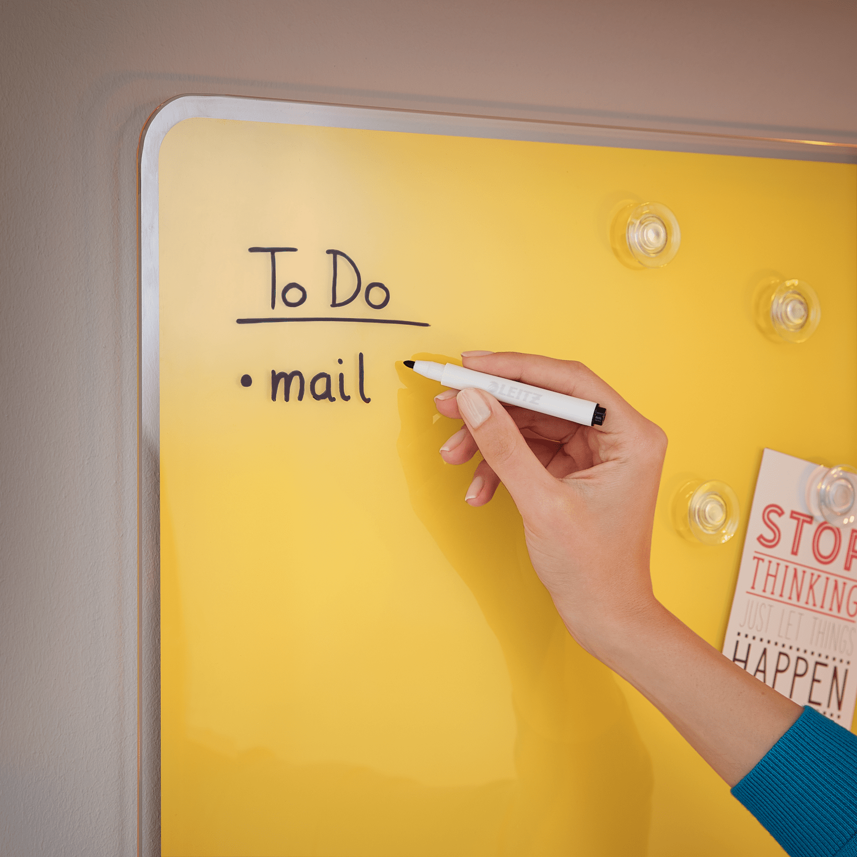 Egy kéz ír egy sárga mágneses táblára. A szöveg: „To Do” és „mail”.