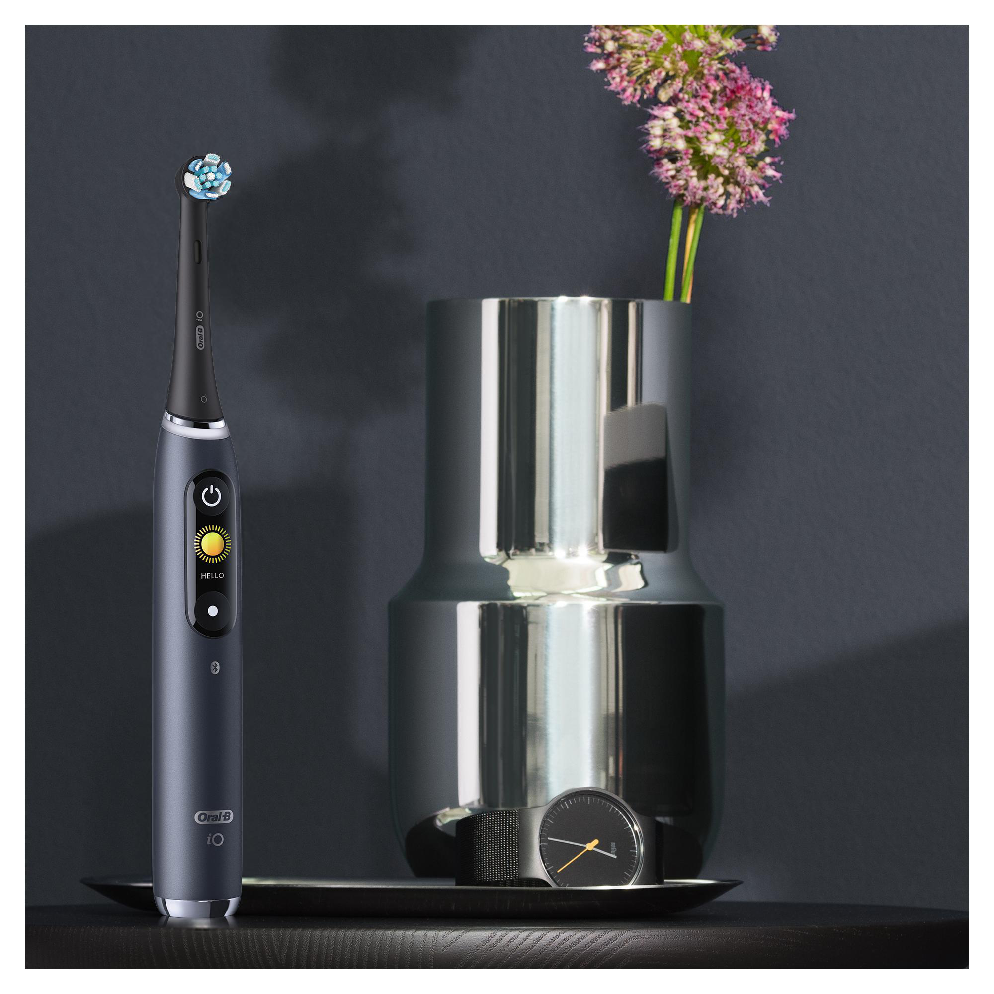 Eine elektrische Zahnbürste Oral-B iO auf einem Tablett mit Vase und Uhr.