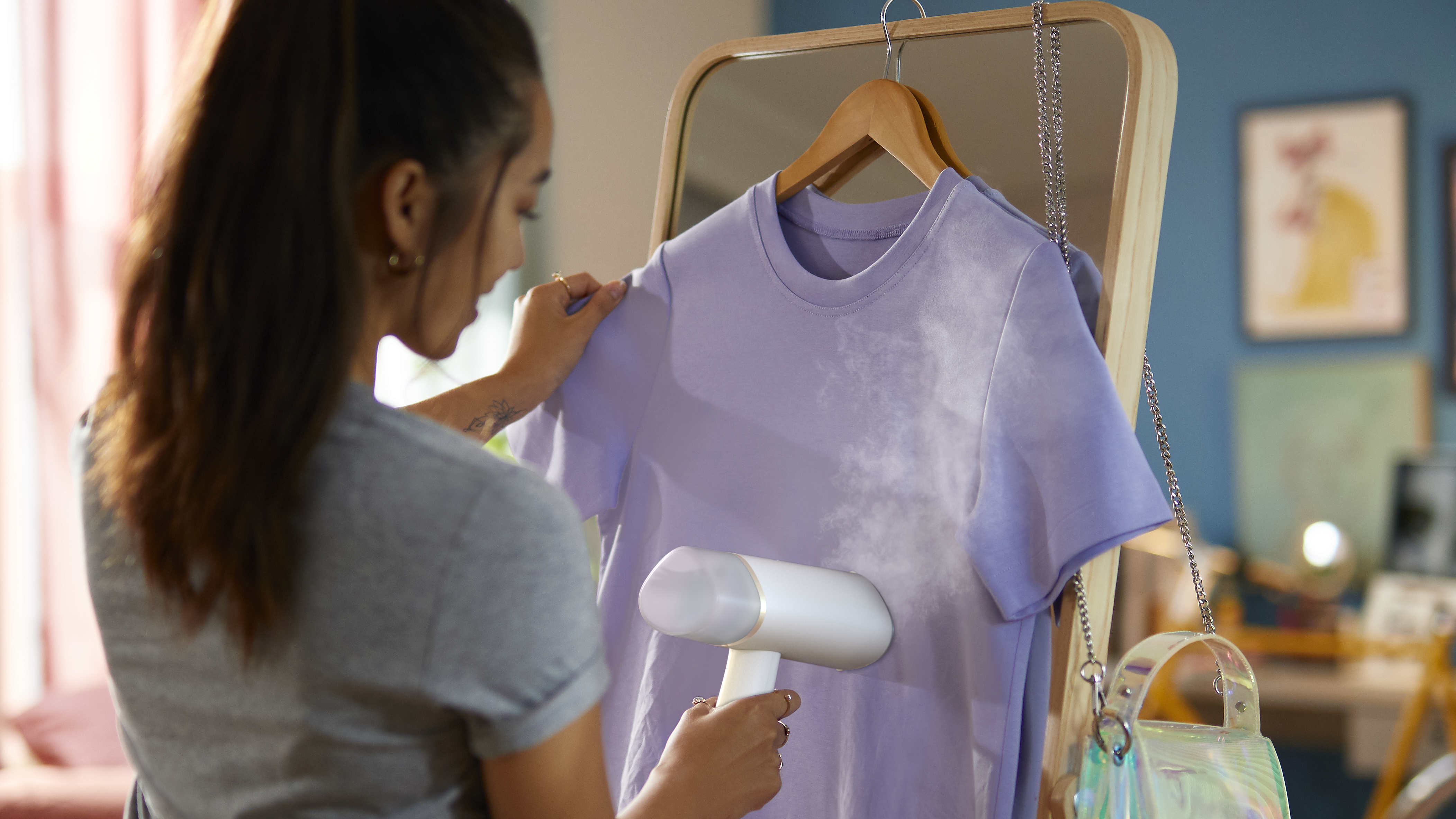 Mujer planchando una camiseta morada en un soporte de espejo, con espejo y fondo.