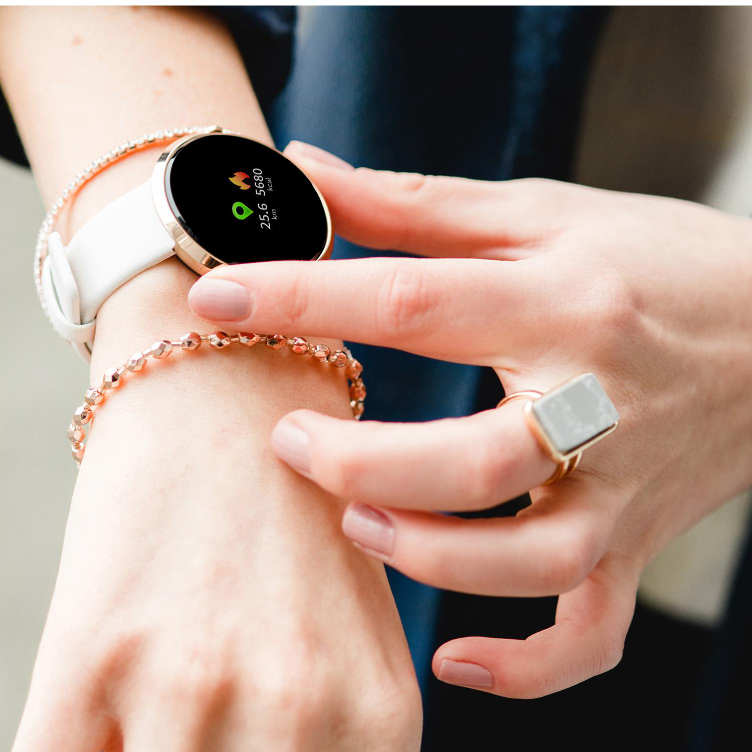 Das Handgelenk einer Frau mit einer weißen Smartwatch, einem Armband und einem Ring wird gezeigt.