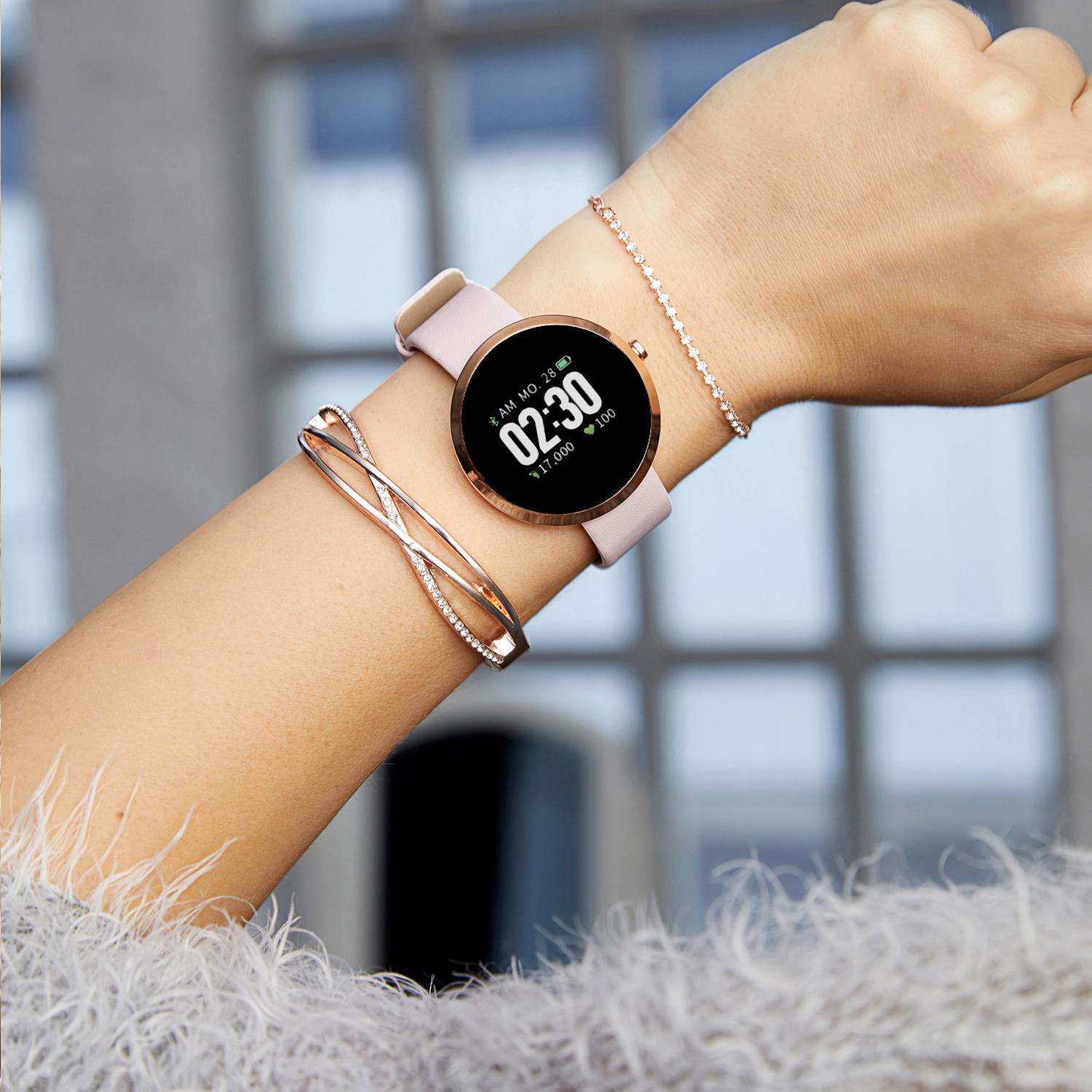 Handgelenk einer Frau mit Smartwatch und zwei Armbändern. Die Uhr ist rosa mit goldenem Rand.