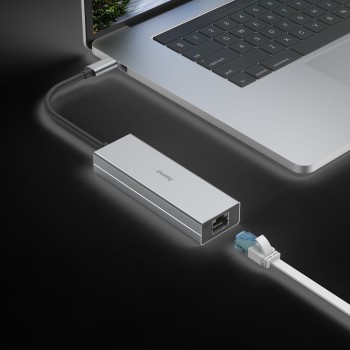 Adaptador concentrador plateado con cable Ethernet azul y blanco conectado a un portátil.