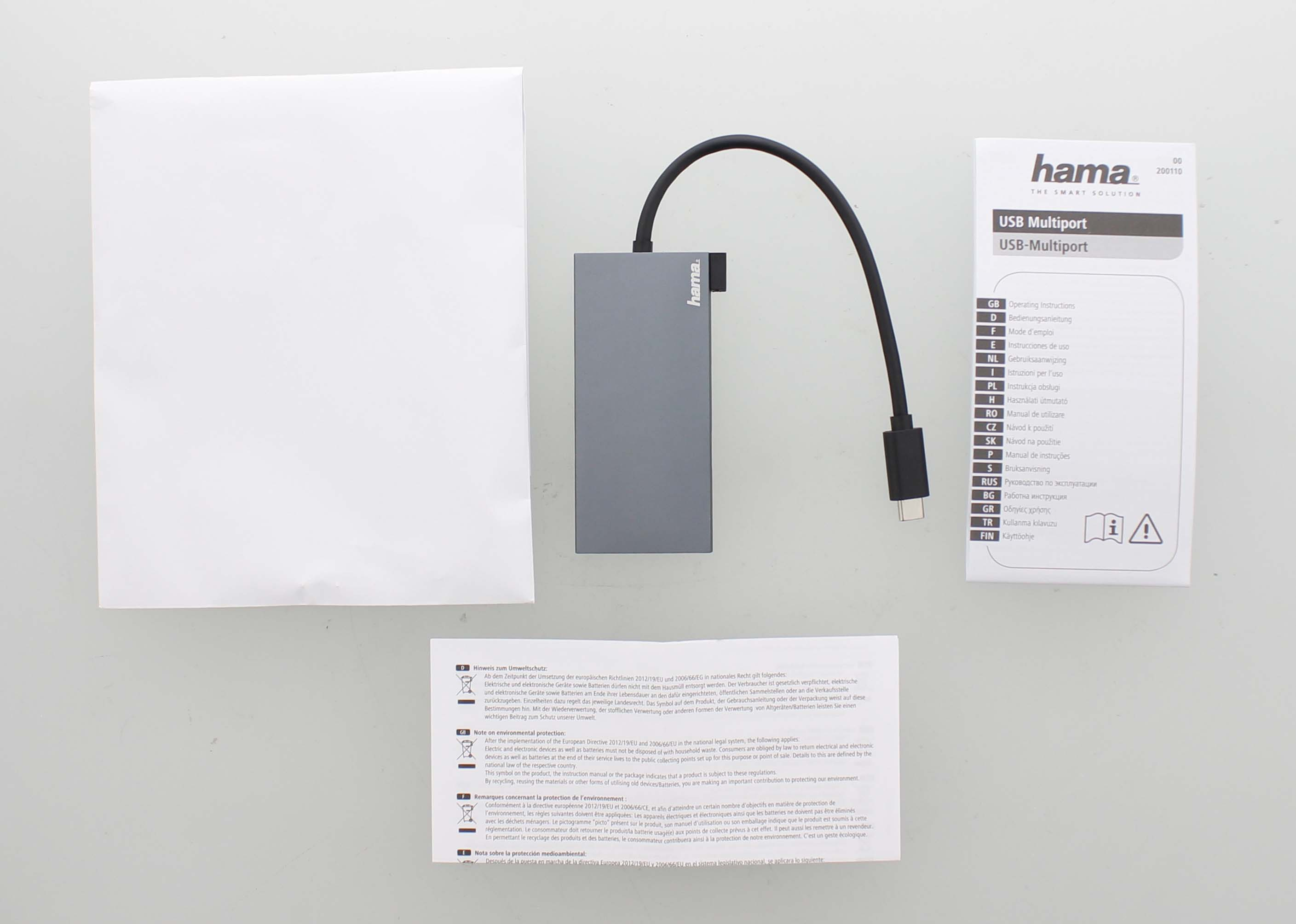 Dispositivo multiport USB con cables, hojas de instrucciones y una caja blanca sobre superficie blanca.
