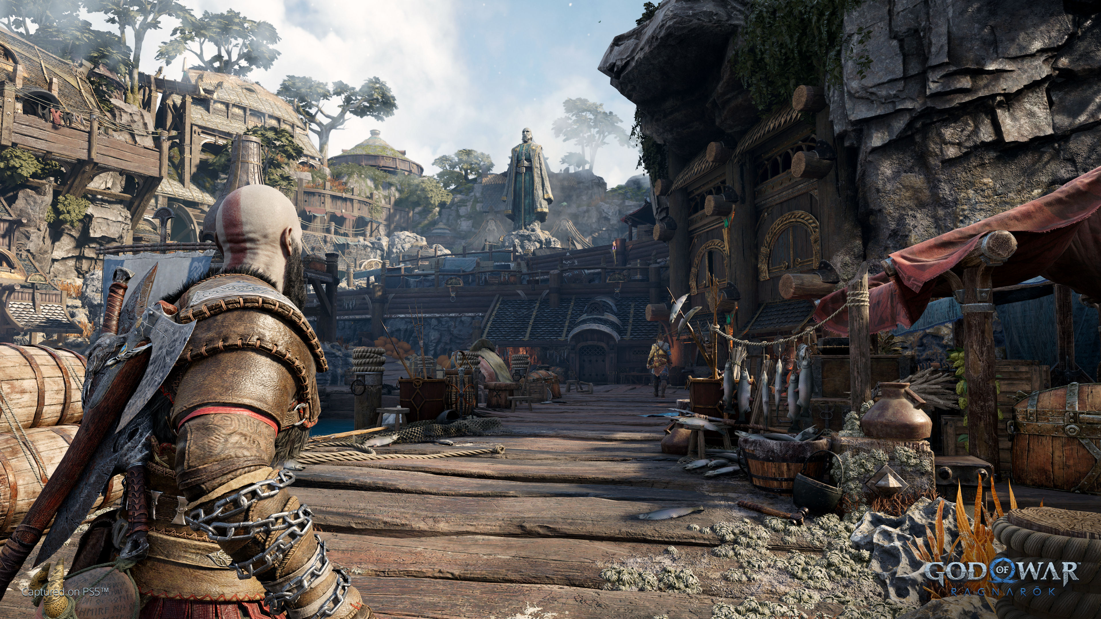 God of War Spielszene mit Kratos, der eine Stadt betrachtet, Statue im Hintergrund.