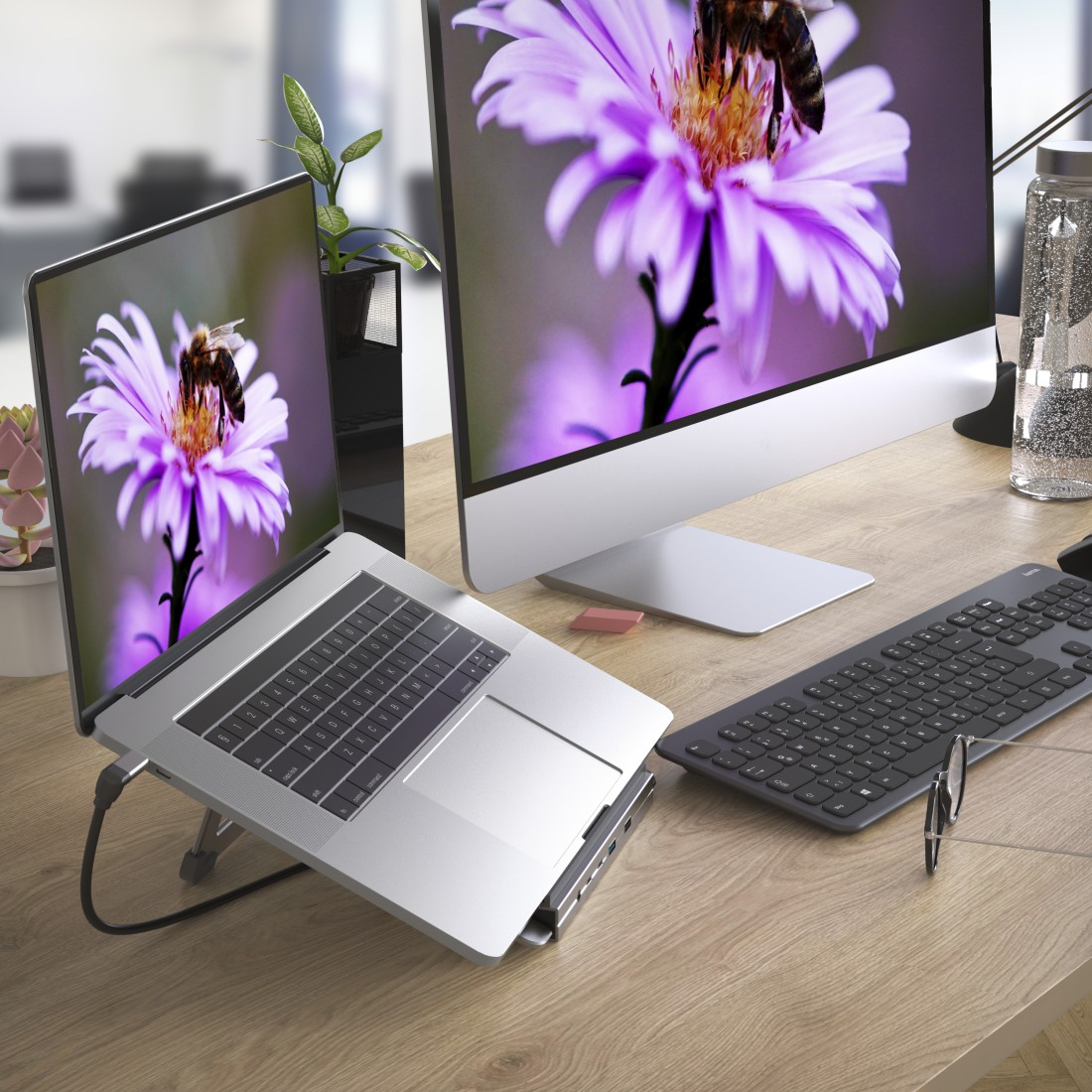 Laptop mit Bienen- und Blumenbild, angeschlossen an einen Monitor, eine Tastatur und eine Wasserflasche.