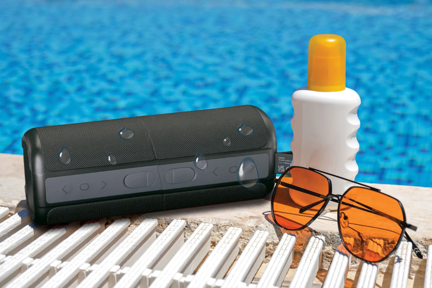 Schwarzer Lautsprecher, Sonnencreme und Sonnenbrille am Pool. Wassertropfen auf Lautsprecher.