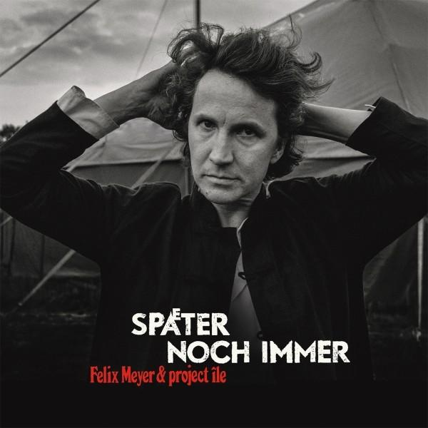 Ein Mann mit Händen am Kopf in einer Schwarz-Weiß-Fotografie. Text 'SPÄTER NOCH IMMER'.