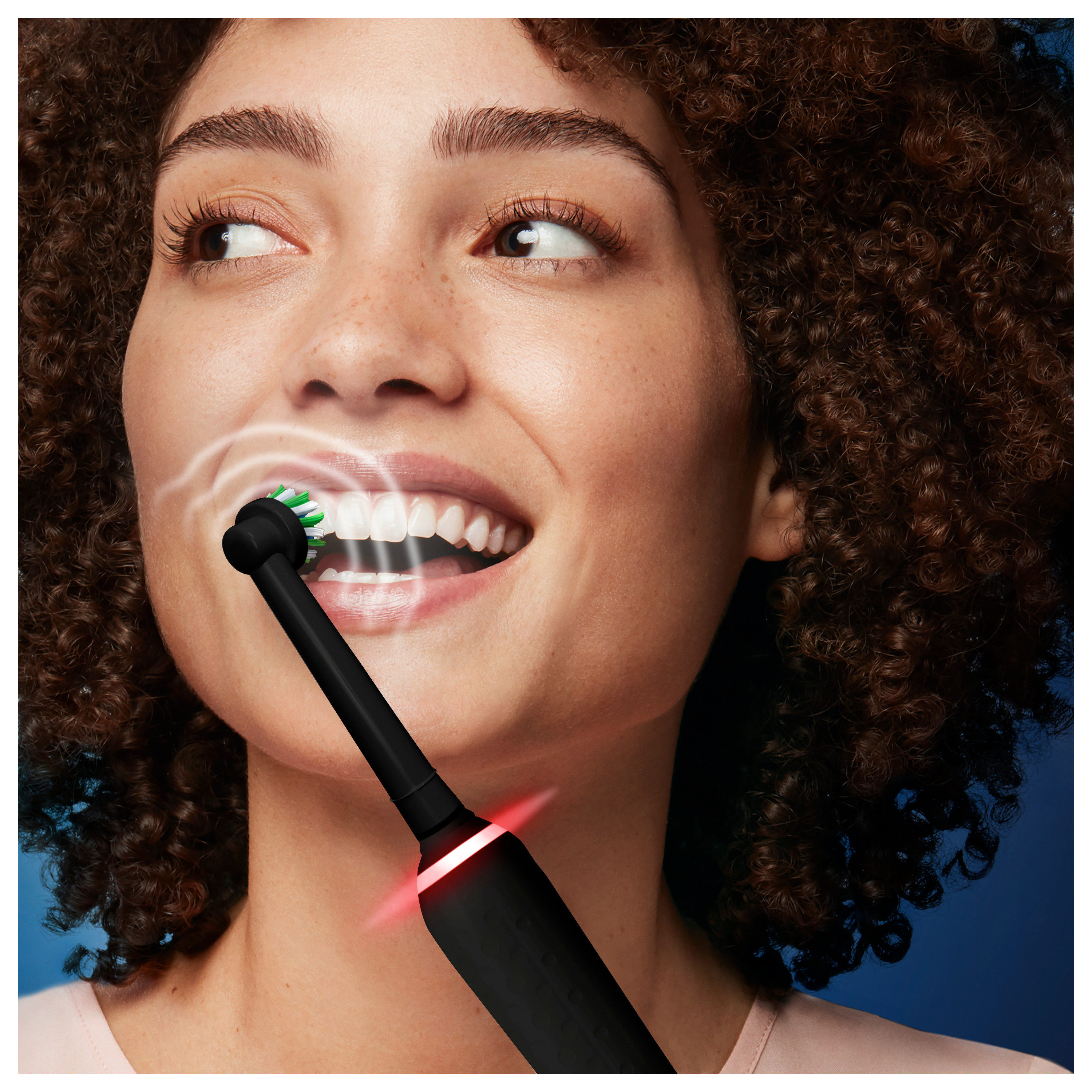 Femme se brossant les dents avec une brosse à dents électrique noire. Mousse blanche et lumière rouge visibles.