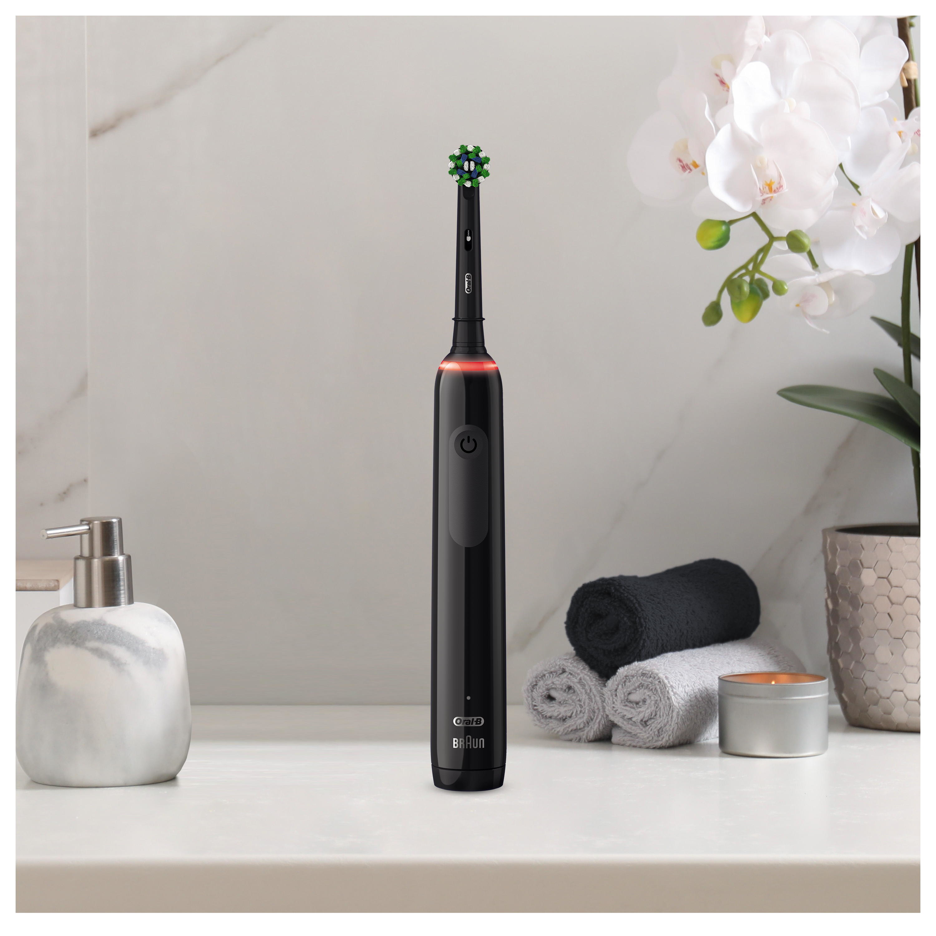 Brosse à dents électrique noire sur un comptoir blanc, à côté d'un distributeur de savon.