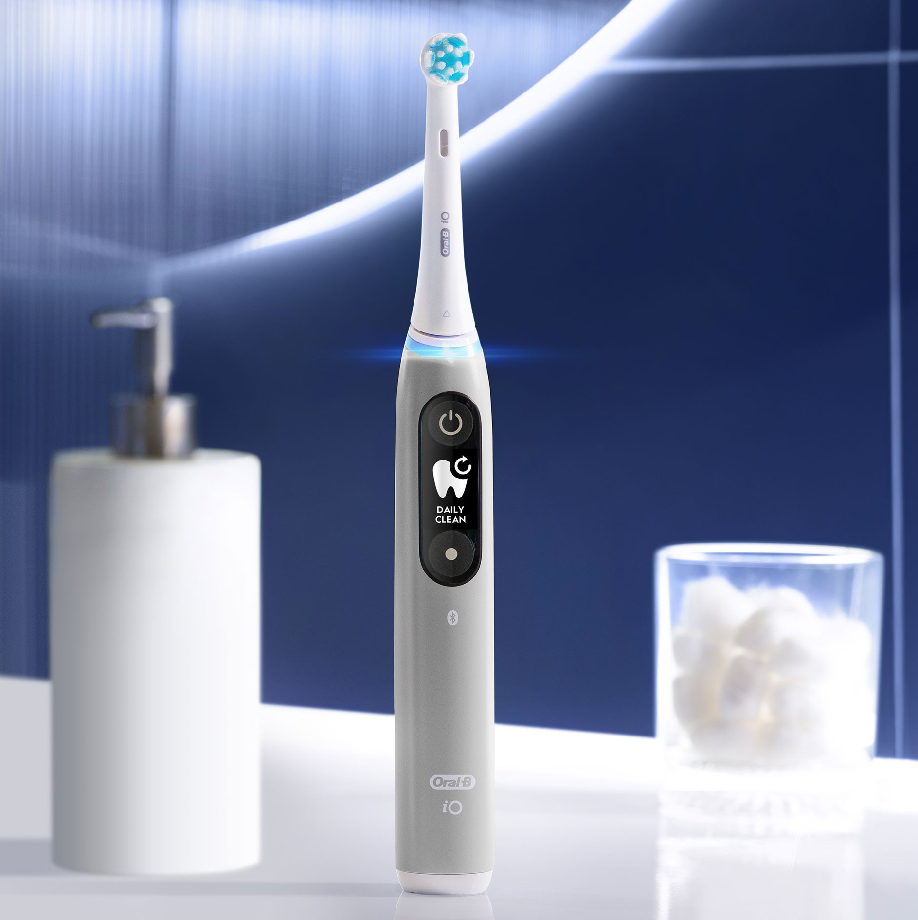 Uno spazzolino elettrico con schermo che mostra 'Daily Clean'. C'è un dispenser di sapone e batuffoli di cotone.