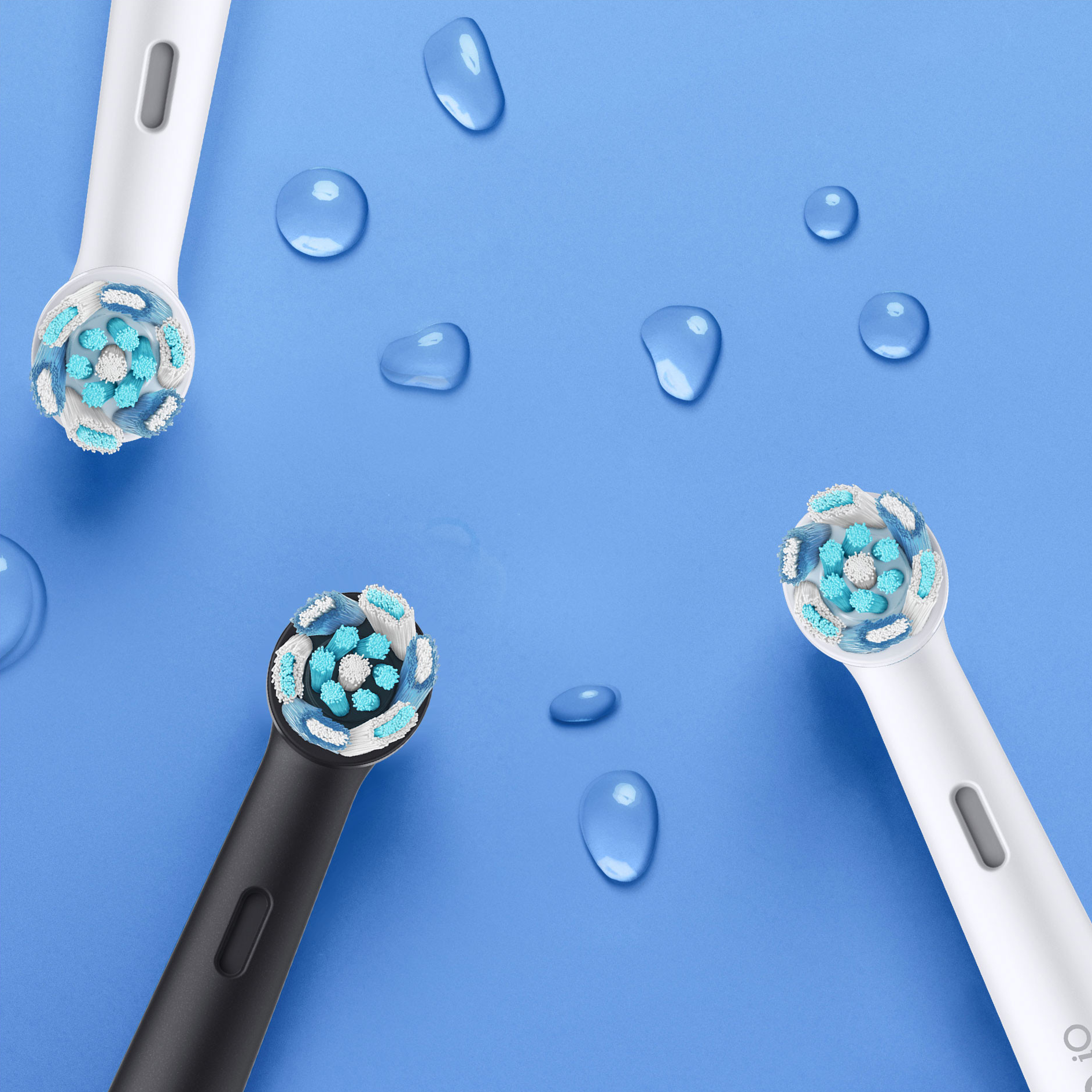 Primo piano di tre testine per spazzolino elettrico e gocce d'acqua su sfondo blu.