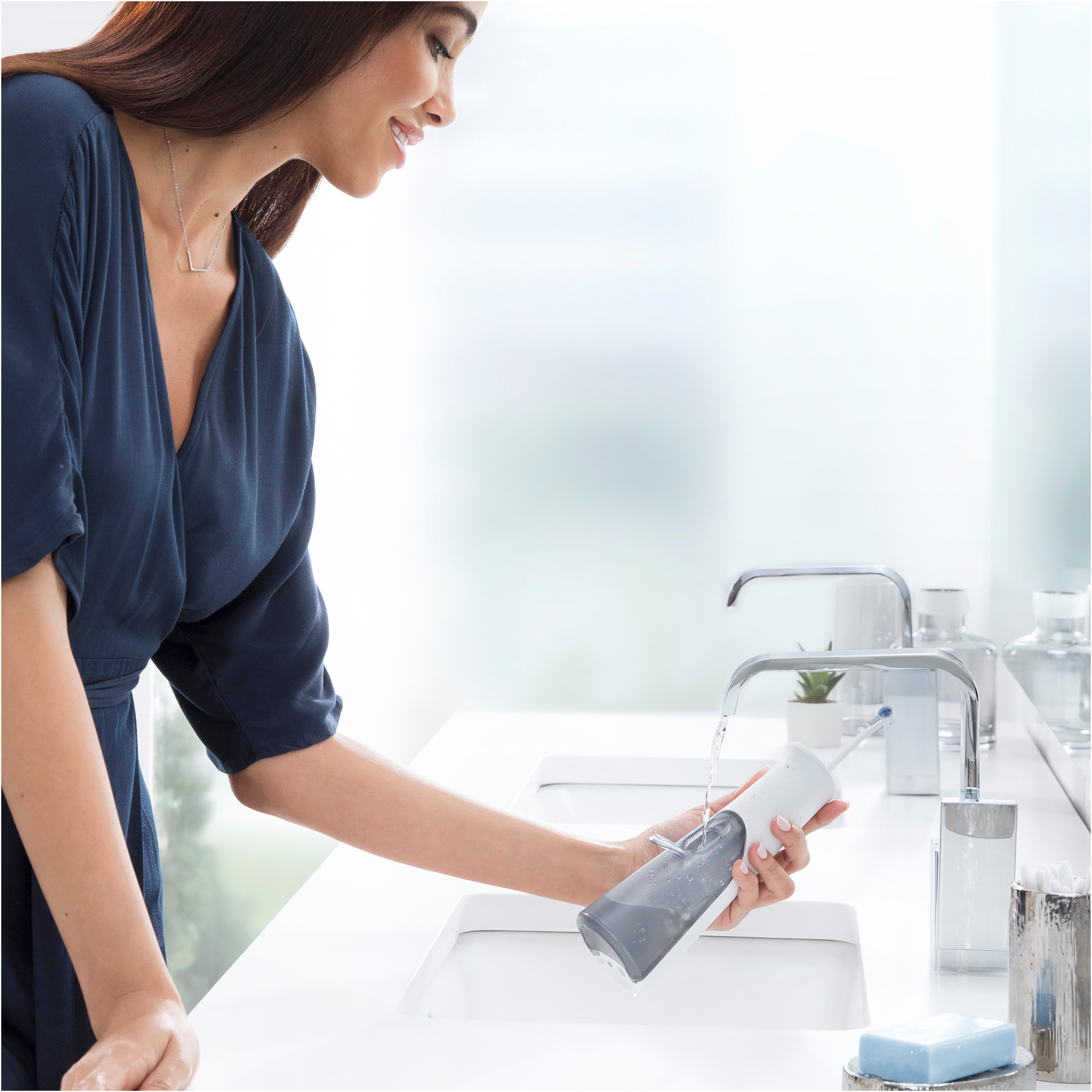 Una donna che usa un idropulsore presso un lavandino bianco del bagno.