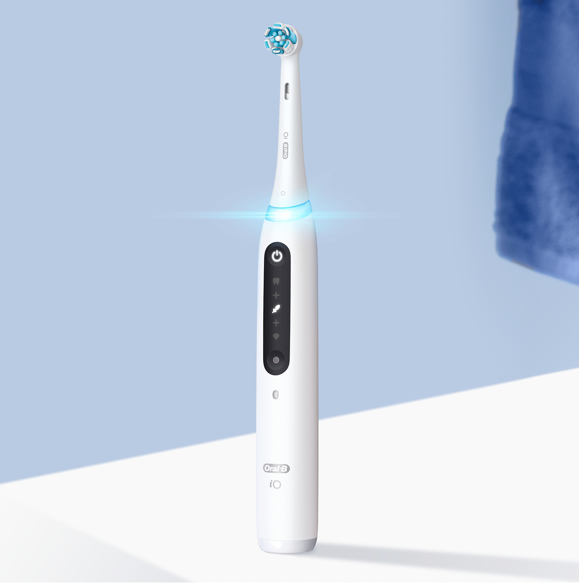 Spazzolino elettrico Oral-B iO bianco. È su una superficie bianca con luce blu e un asciugamano blu.