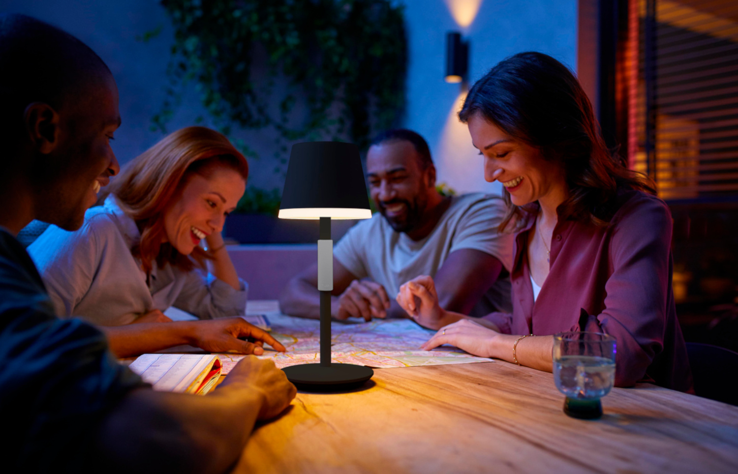 Group of people around a table with a lamp, looking at a map, in a night scene.